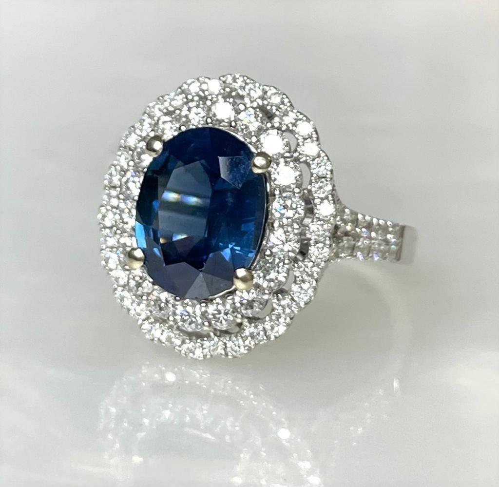 A traditional and luxurious blue sapphire ring set in solid 18k white gold. Featuring an oval shaped center stone weighing 3.80 carats surrounded by 1.02 carats of sparkling white diamonds forming a double halo and continuing along the