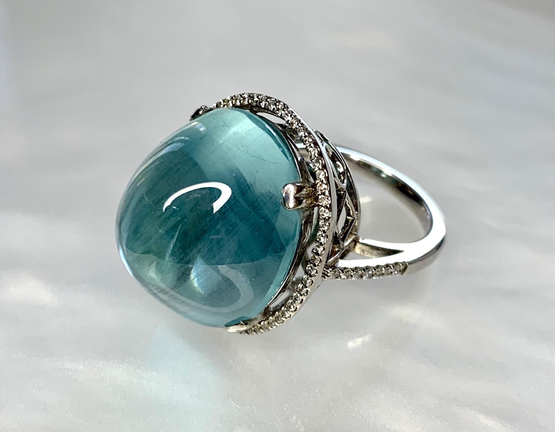 A captivating and luxurious sea- foam green aquamarine piece reminiscent of the first steps we take into the clear blue ocean waters. This super sized cocktail ring featuring a high domed 24.21 carat cabochon center stone surrounded by a halo of