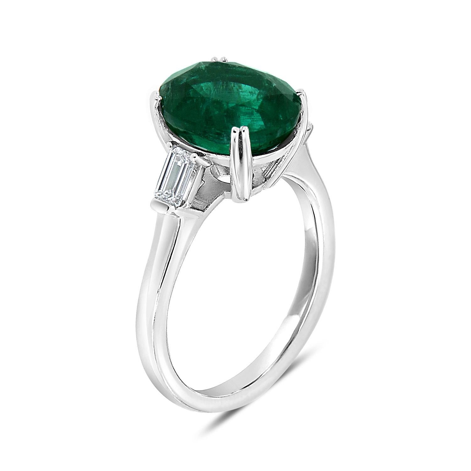 This timeless design Three-Stone ring features a 4.27 Carat Oval-Shape vibrant green Natural Emerald from Zambia flanked by two Emerald shaped natural diamonds in weight of 0.38 Carat on a 2.4 mm band. The Emerald exhibit an exceptional luster. You