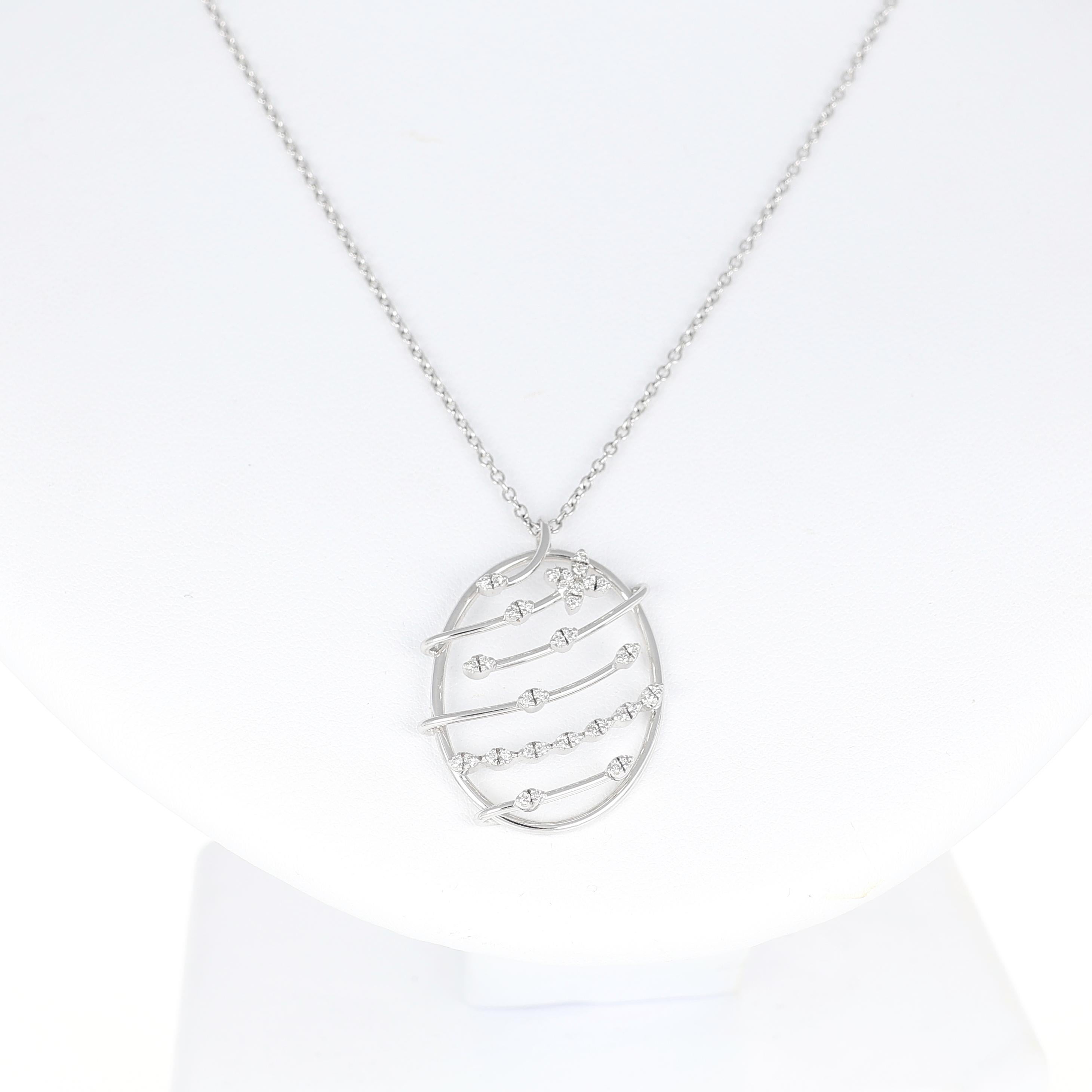 Dal design delicato e contemporaneo, questo pendente in oro bianco 18 carati presenta una struttura ovale traforata ornata da un elegante motivo floreale con diamanti taglio brillante per un totale di 0,23 carati. Le linee fluide del pendente creano