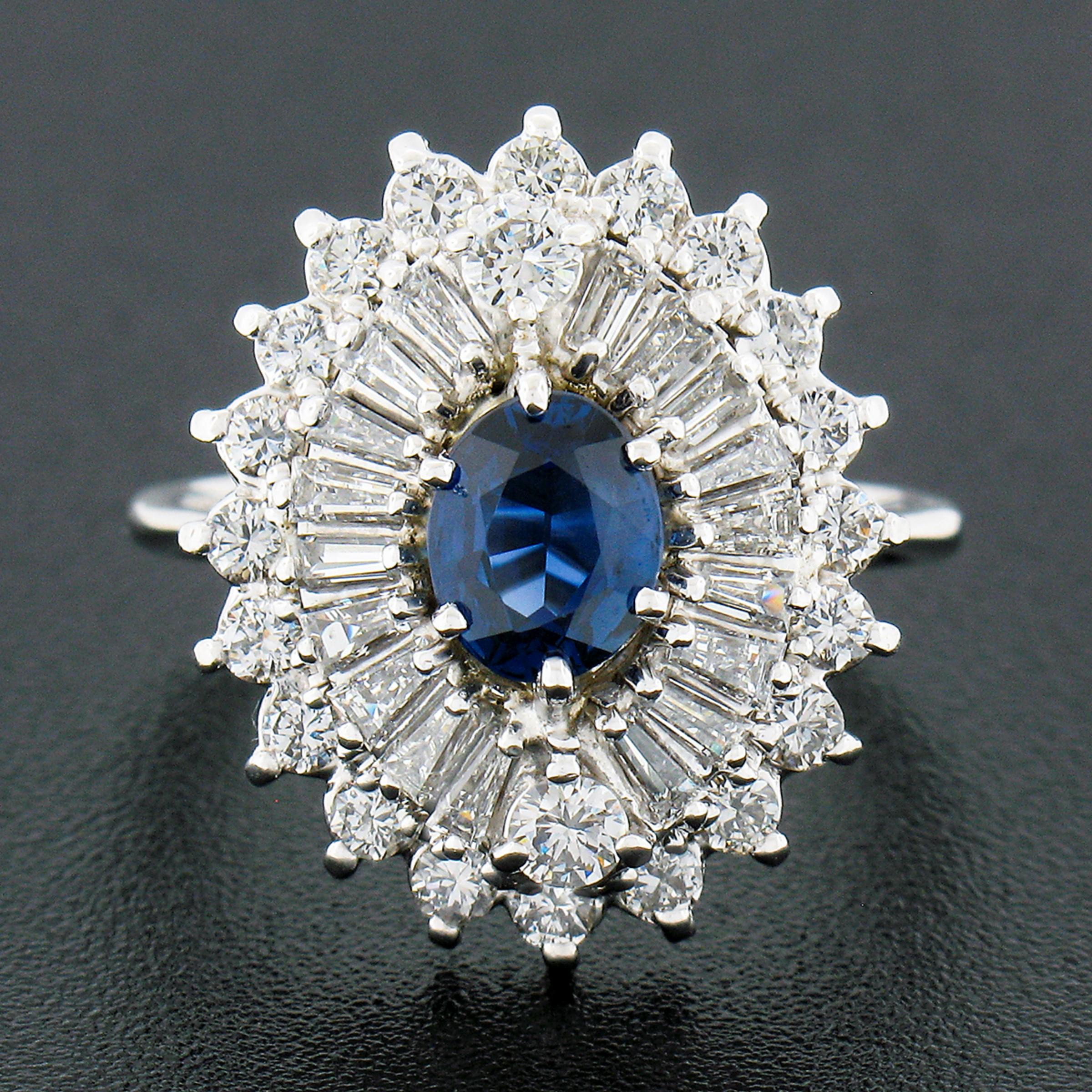 This absolutely stunning, ballerina style cocktail ring is crafted in solid 18k white gold. It features a gorgeous, oval cut, natural sapphire stone neatly prong set at its center displaying a beautiful blue color with amazing shine due to its