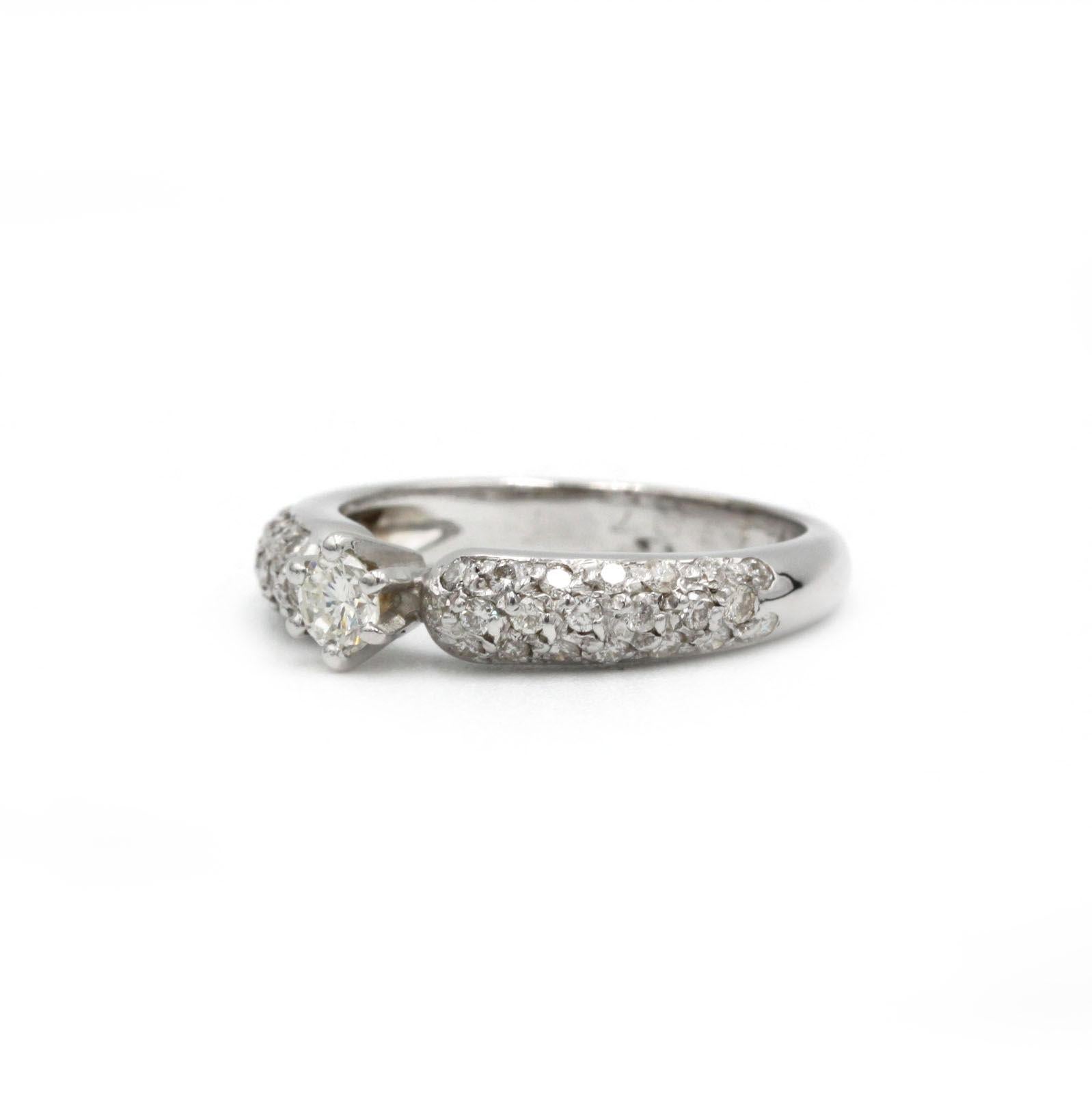 Cette bague contemporaine saisissante associe un diamant central de 0,20 ct de taille brillant à 42 diamants d'accentuation sertis en pavé (~0,50 ct au total) pour créer un jeu de lumière éblouissant sur le doigt. Réalisé en or blanc 18 carats, le
