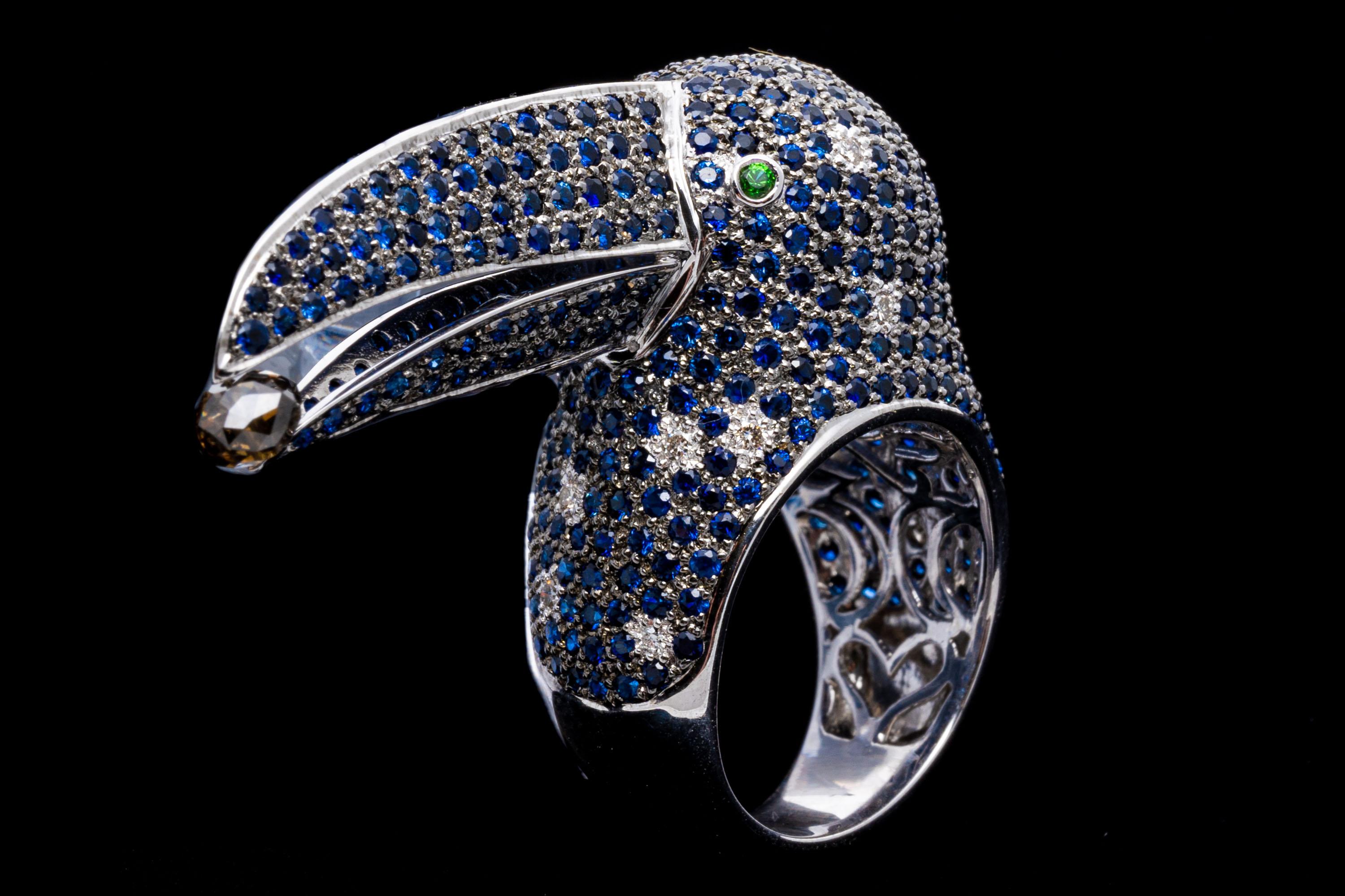 18k white gold ring. This phenomenal ring is a toucan motif, pave set with a field of round faceted, medium blue color sapphires, approximately 4.38 TCW and adorned with scattered round faceted diamonds, approximately 0.15 TCW. The face of the