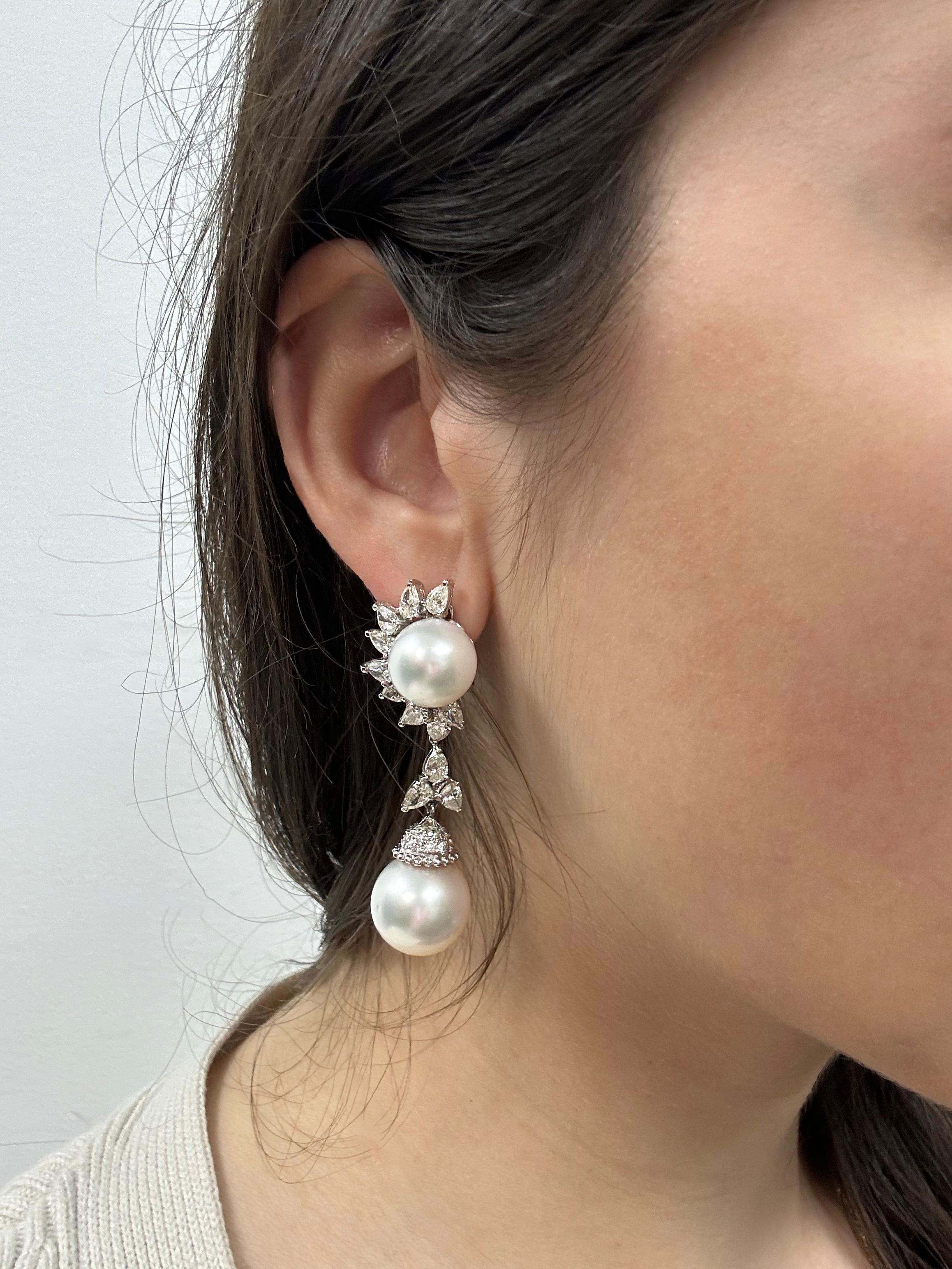 Ces élégantes boucles d'oreilles pendantes en or blanc 18 carats présentent une paire de perles lumineuses encadrées par un arrangement en demi-soleil de diamants taille poire. Le motif tombe en cascade dans une deuxième goutte de perle accentuée de