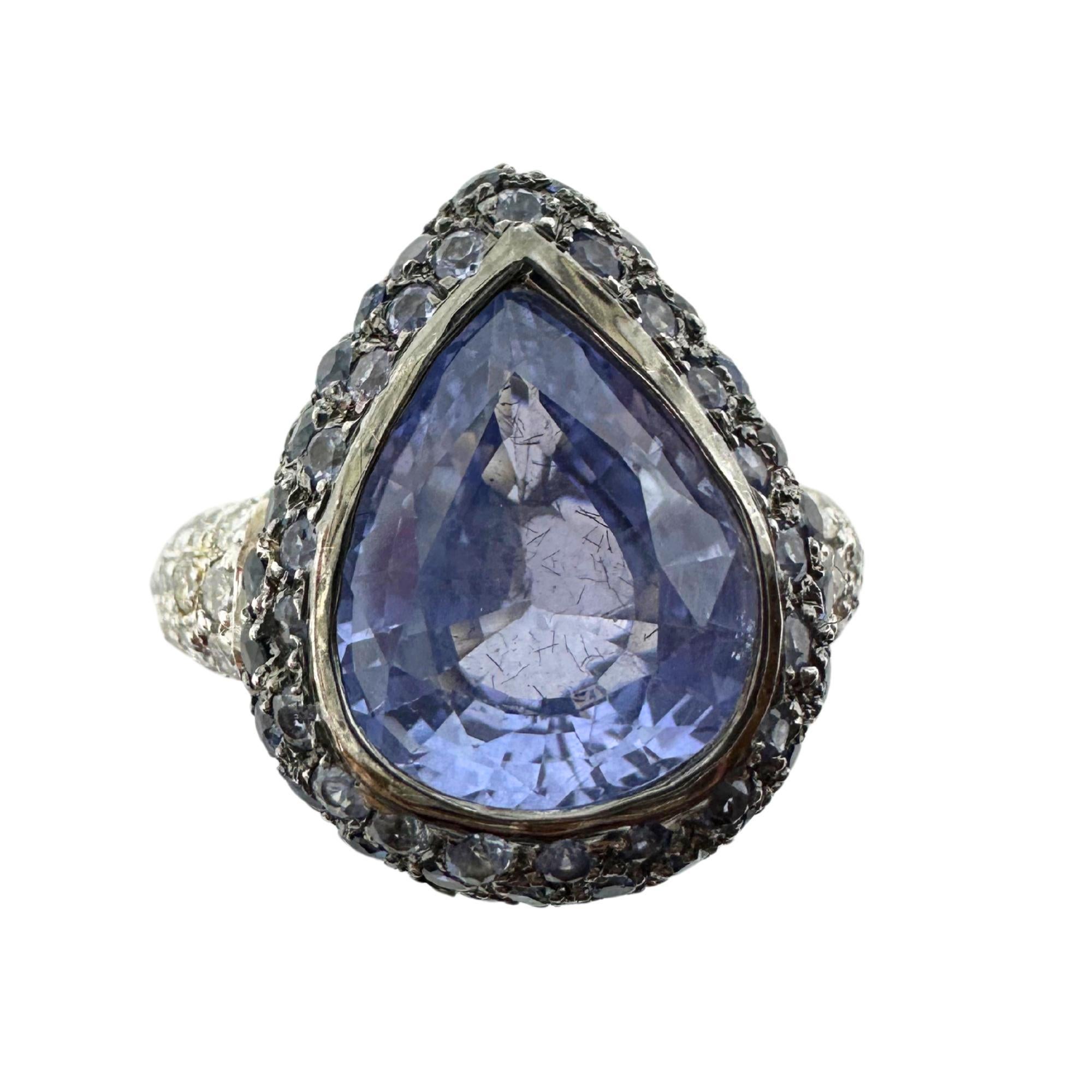 Cette bague en or blanc 18 carats, qui constitue une superbe pièce d'apparat, présente en son centre un saphir hypnotique de 5,15 carats taillé en poire, entouré d'un halo étincelant d'accents de saphir pesant 2,01 carats. Le design est rehaussé de