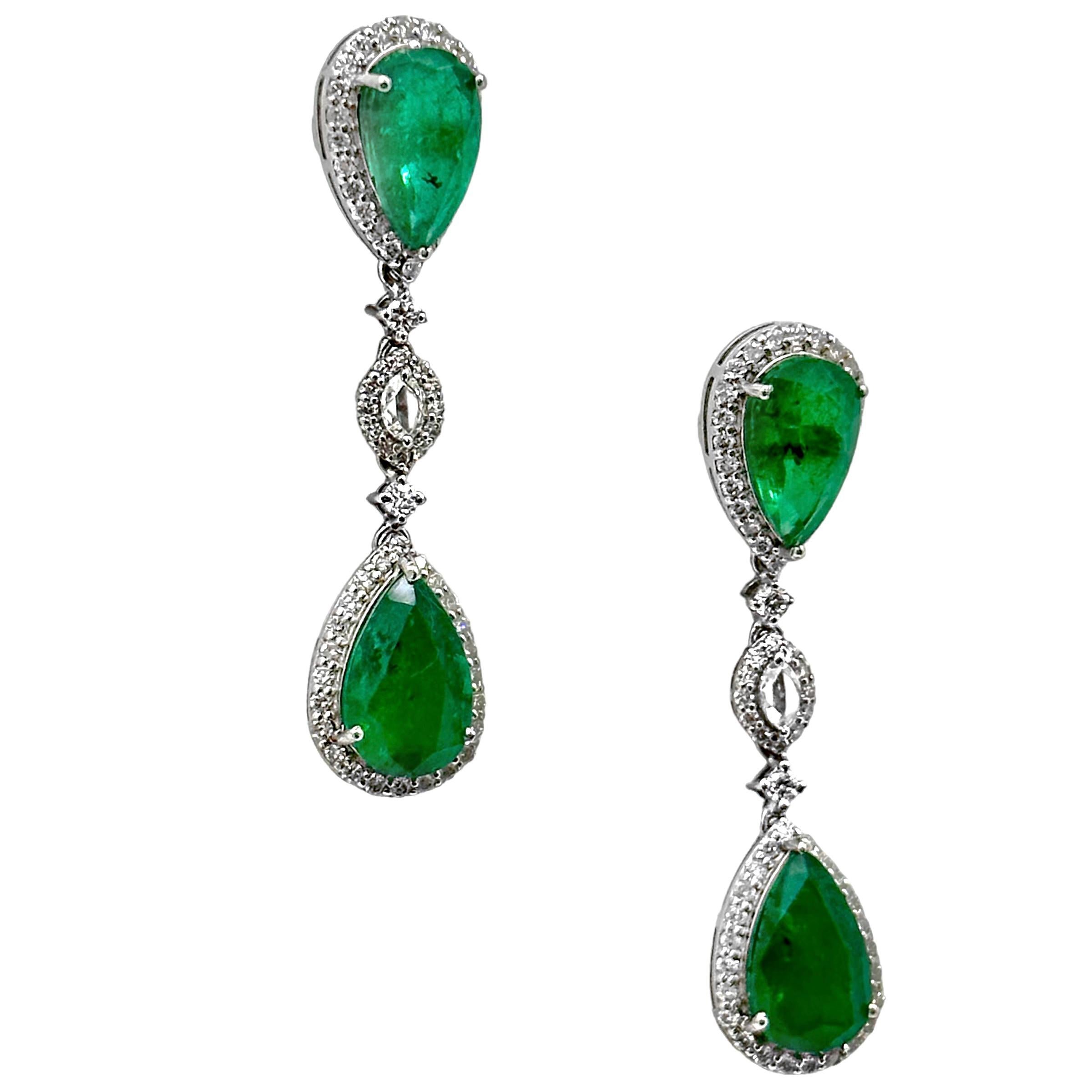 A pair of 18K white gold earrings set with four pear-shaped, vibrant emeralds, surrounded by diamonds. Measuring 1 3/4 inches long, they have an elegant appearance. The total weight of the emeralds is approximately 8.66ct, which pairs perfectly with