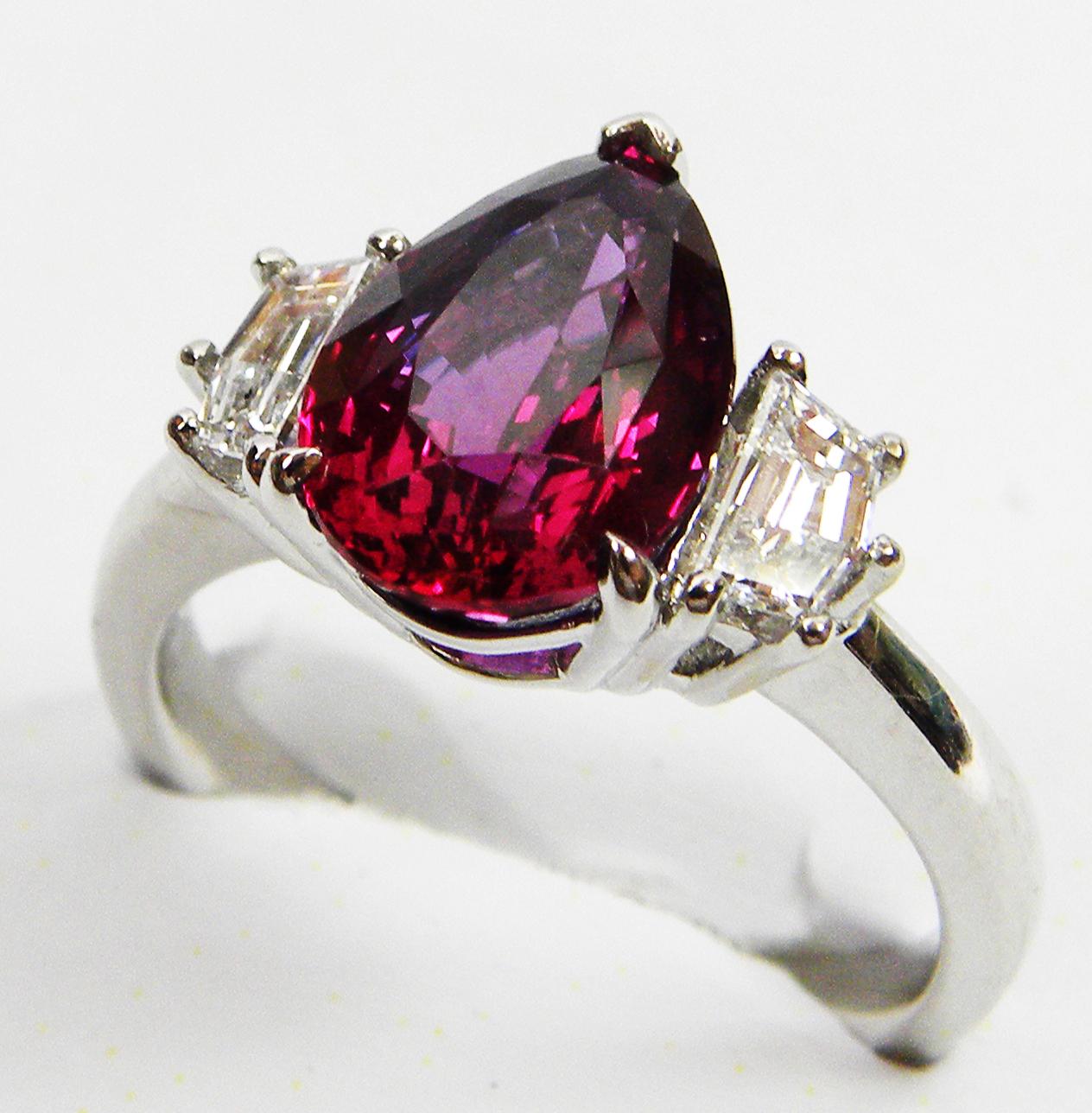 
At its heart lies a breathtaking 3.40 ct pear-shaped ruby, showcasing a vibrant orangy-red hue, sourced from the world-renowned ruby mines of Mozambique, and accompanied by a GRS certification. 

The two fancy-shaped diamonds (0.49 cts) sparkle