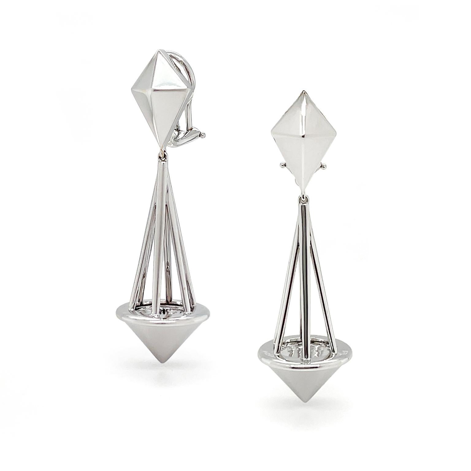 Luminance amplifies this geometric ensemble. The design begins with a kite raised in shape for dimension. From this, drops four slender bars which form a pendulum. The pendulum attaches to a downward-turned cone. The earrings are composed entirely