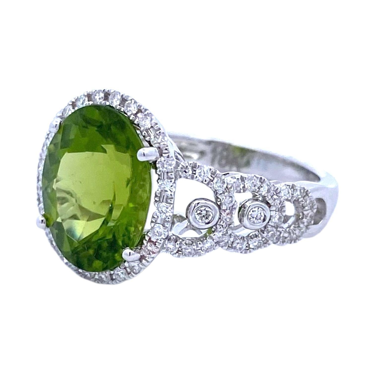 Crafted in 18K white gold, the ring showcases a striking oval-cut peridot at its center. The vibrant green stone is encircled by brilliant-cut diamonds, and the band is adorned with additional diamond accents, enhancing its luxurious appeal. The