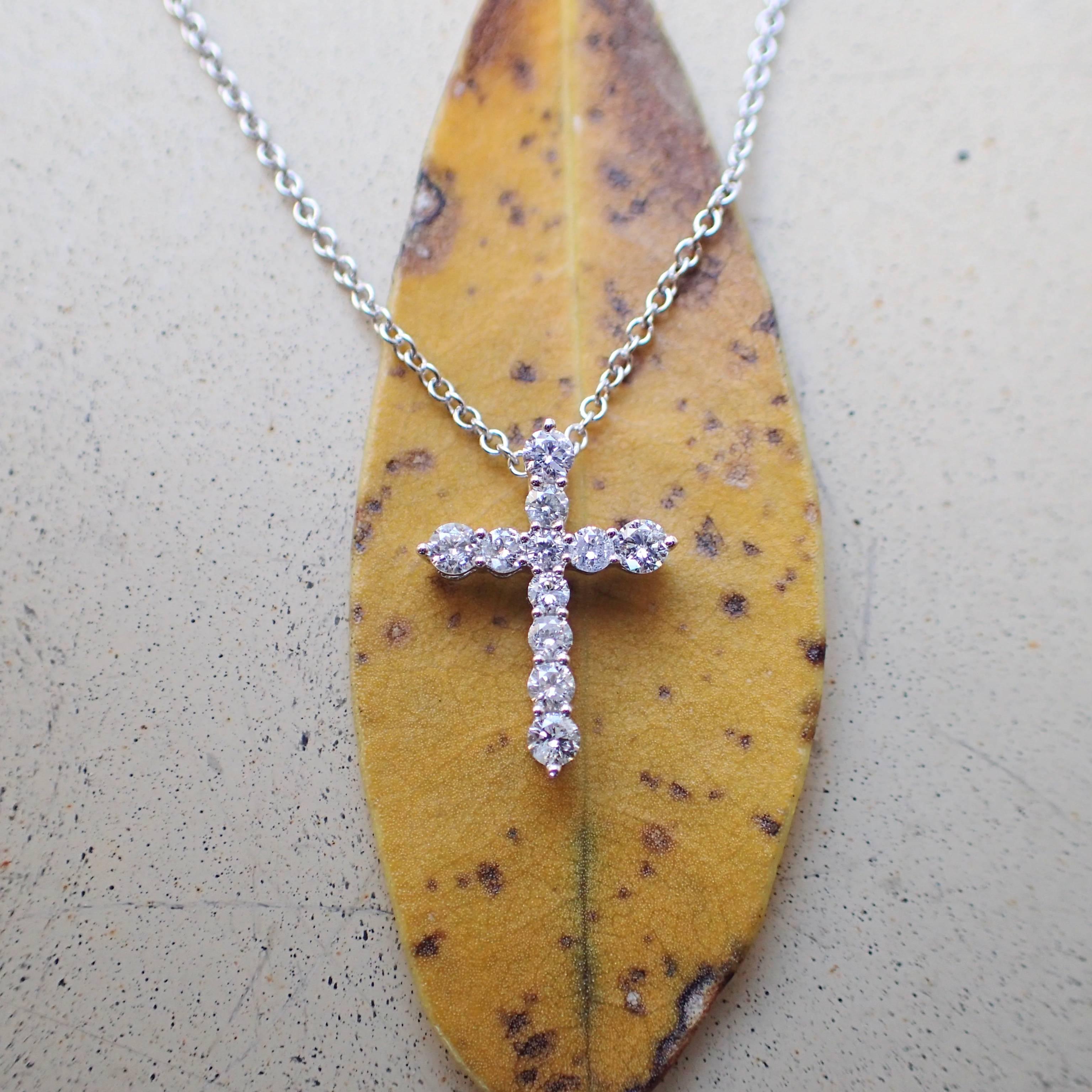 18k white gold thin cross with eleven (11) Round Brilliant Cut diamonds weighing a total of 0.247 carats with Color Grade G and Clarity Grade VS. The cross weighs 0.38 grams. The cross measures 13.36mm in length and 9.8mm in width. The cross hangs