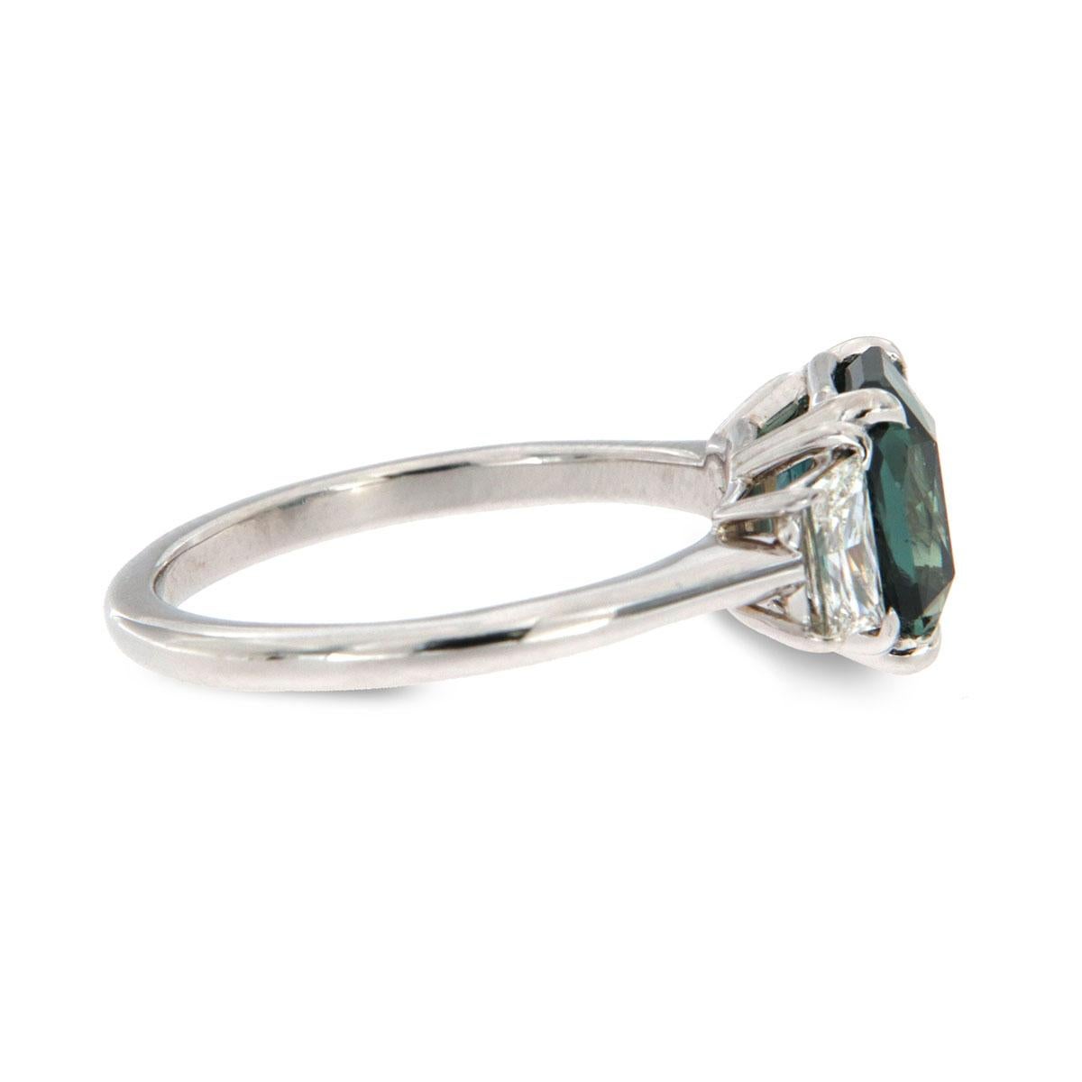 This timeless design is a unique Trilogy ring that showcases a Rare Radiant shape 2.92 Teal color Sapphire Unheated GIA Certificate 1206137505 flanked by two Trapazoite diamonds in a total weight of 0.53 Carat—handcrafted in 18k white gold. The ring