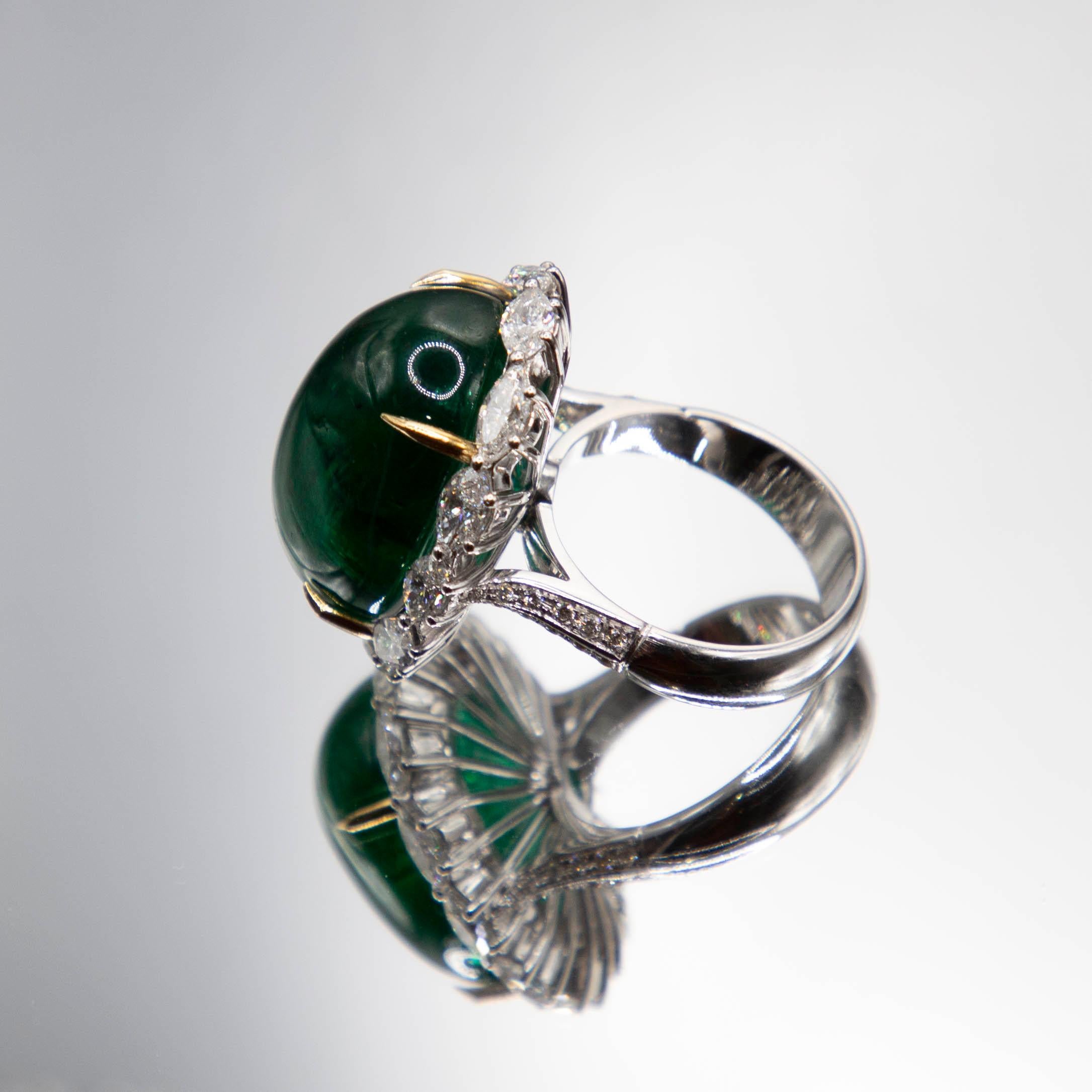 A rare and intense deep green 27.85 carat Zambian emerald displays alluring transparency in a one of a kind 18k white gold, handmade ring. Four talon-style prongs of 18k yellow gold hold the gem securely. Expertly-cut marquise diamonds trace the