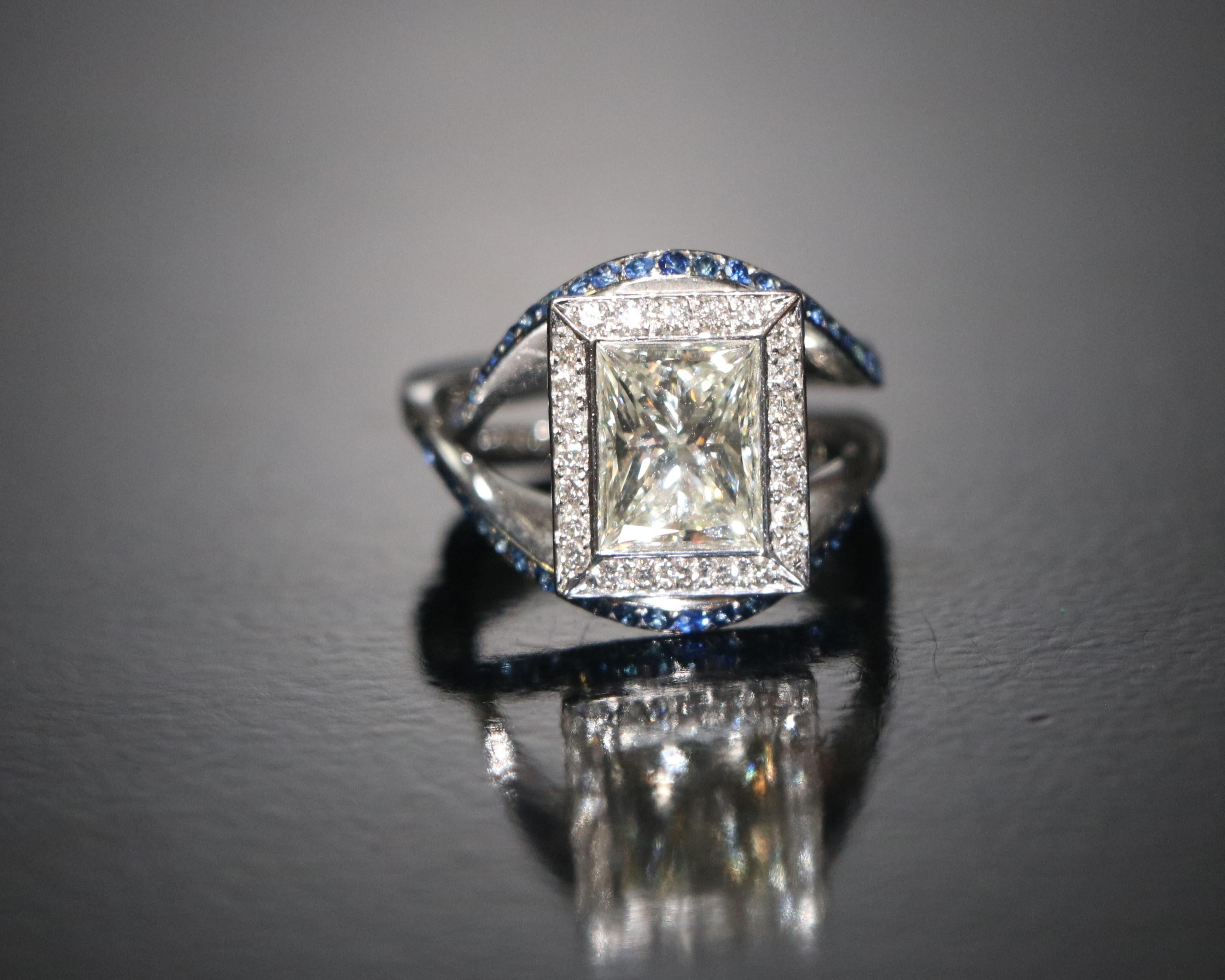 Anello in oro con diamanti e zaffiri

Materiale: oro bianco 18 carati

Pietra centrale:
Un diamante di circa 9,64 × 7,56 × 5,45 mm.
Il diamante pesa circa 3,5 carati.
Forma di taglio: Radiante
Pulizia: H. H. vs. H.

Intarsio esterno: 
Dimensioni dei