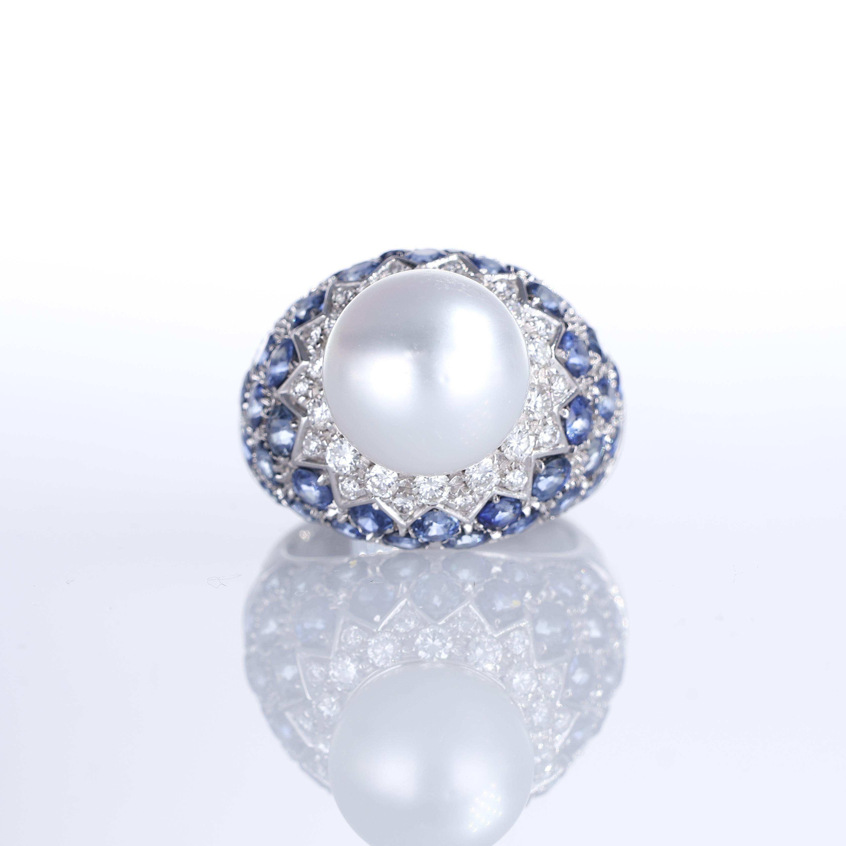 An elegant 18K white gold ring featuring a luminous central pearl, set against a striking pavé of round-cut diamonds and deep blue sapphires. The intricate design combines 0.78 carats of brilliant-cut diamonds with 5.95 carats of sapphires, creating