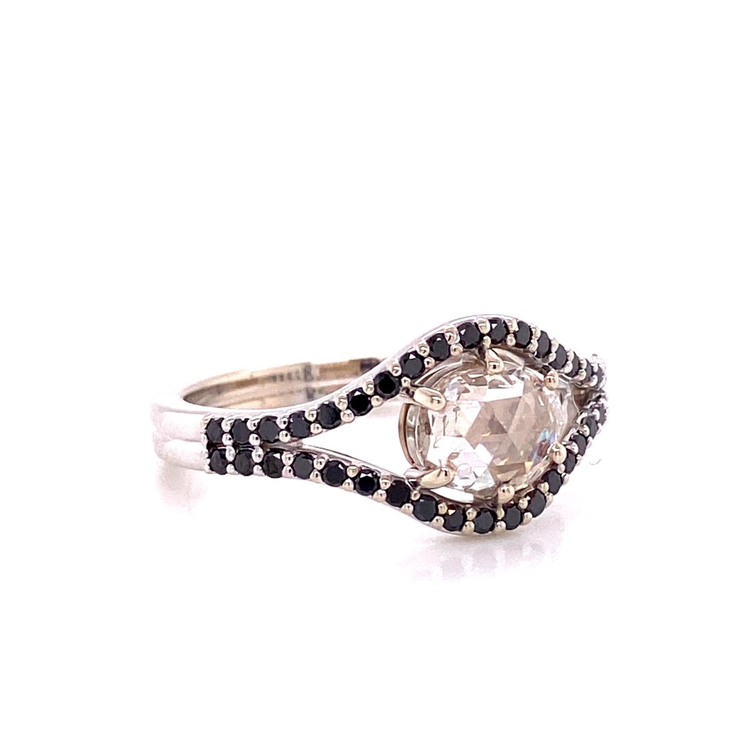 An 18k white gold ring featuring one prong set rose cut oval white diamond, 0.80 carats, and two surrounding rows of round full cut black diamonds, 0.28 total carat weight. Ring size 7. This ring was custom designed and made by llyn strong.