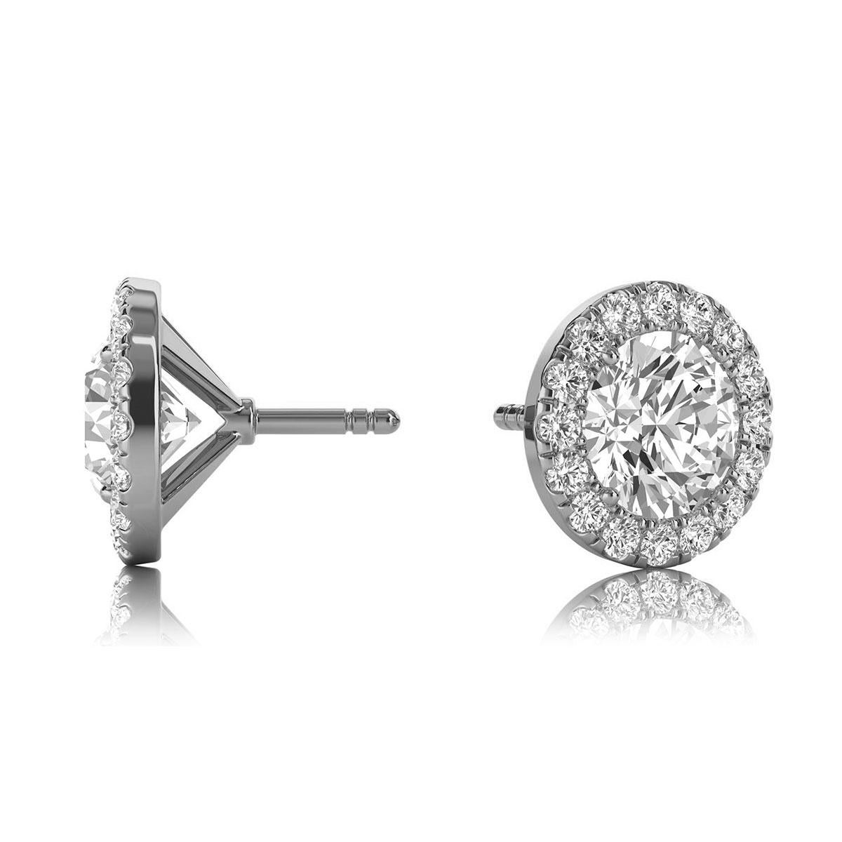 These delicate earrings feature two round shaped diamonds that are approximately 1.08-carat total weight (5.2 mm) encircled by a halo of perfectly matched 32 round brilliant diamonds in about 0.32-carat total weight. The earrings are measuring at 8