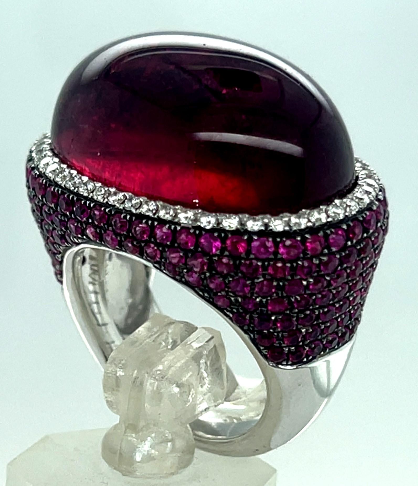 Gorgeous, Unique Rubellite Cabochon Ring
Features Oval Cabochon-Cut Rubellite Set Horizontally
Appx Dimensions = 24.71 mm x 16.32 mm (Appx 25 ct)
Features Diamond Bezel Around Rubellite
Features Pave Ruby Accent Stones on Shoulders
Width of Band = 5