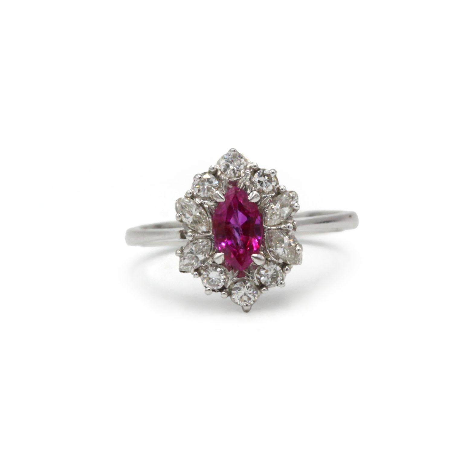 This elegant cluster ring is crafted in 18K white gold and features a vivid marquise-cut ruby at its center, framed by a halo of sparkling brilliant-cut diamonds. The deep pink-red ruby creates a striking contrast against the bright, lively