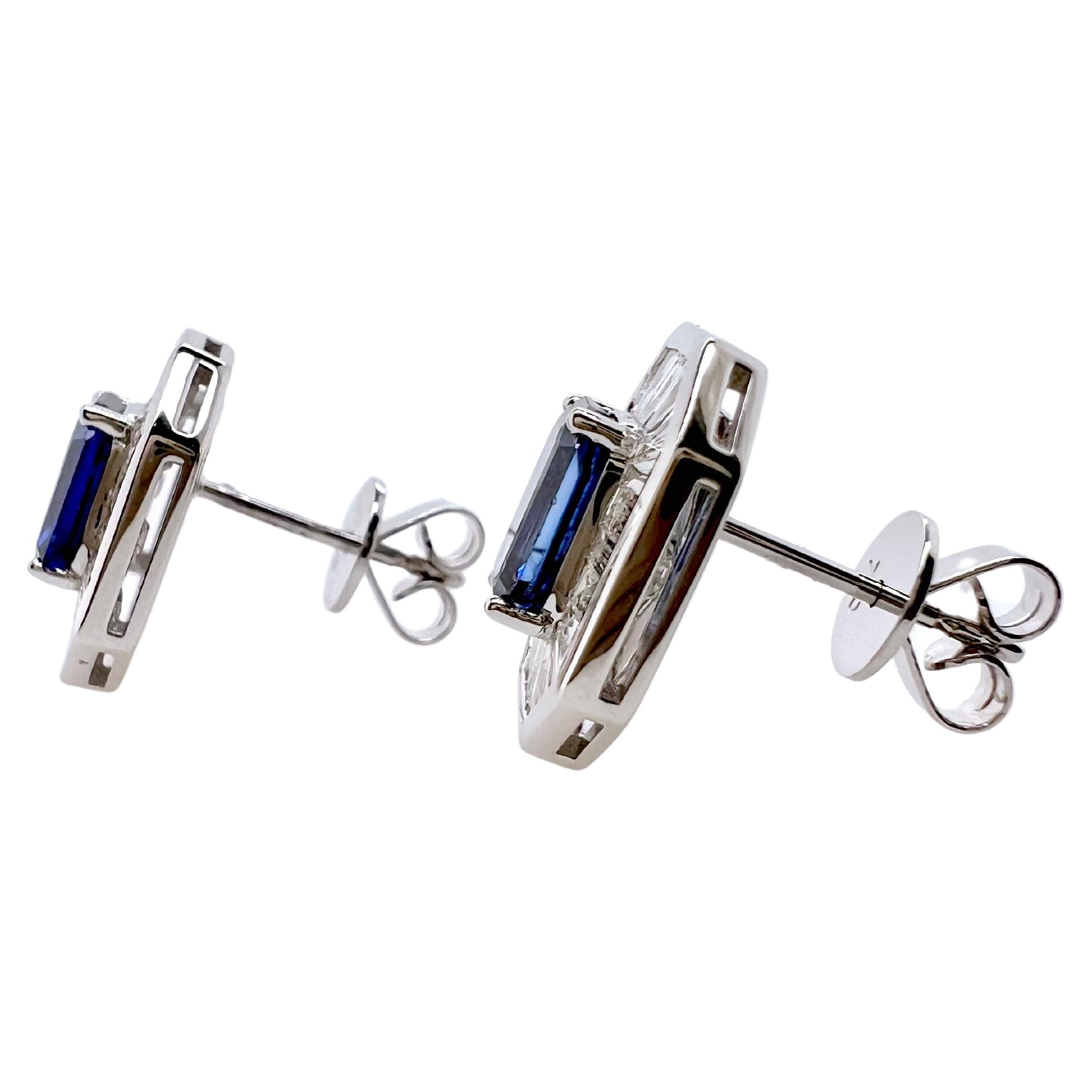This gorgeous pair of emerald cut blue sapphire are surrounded by stunning diamond baguettes in 18k white gold . 
 The baguettes and frame of the earrings mimic and accentuate the shape of the emerald cut, royal blue colored sapphire.  These are