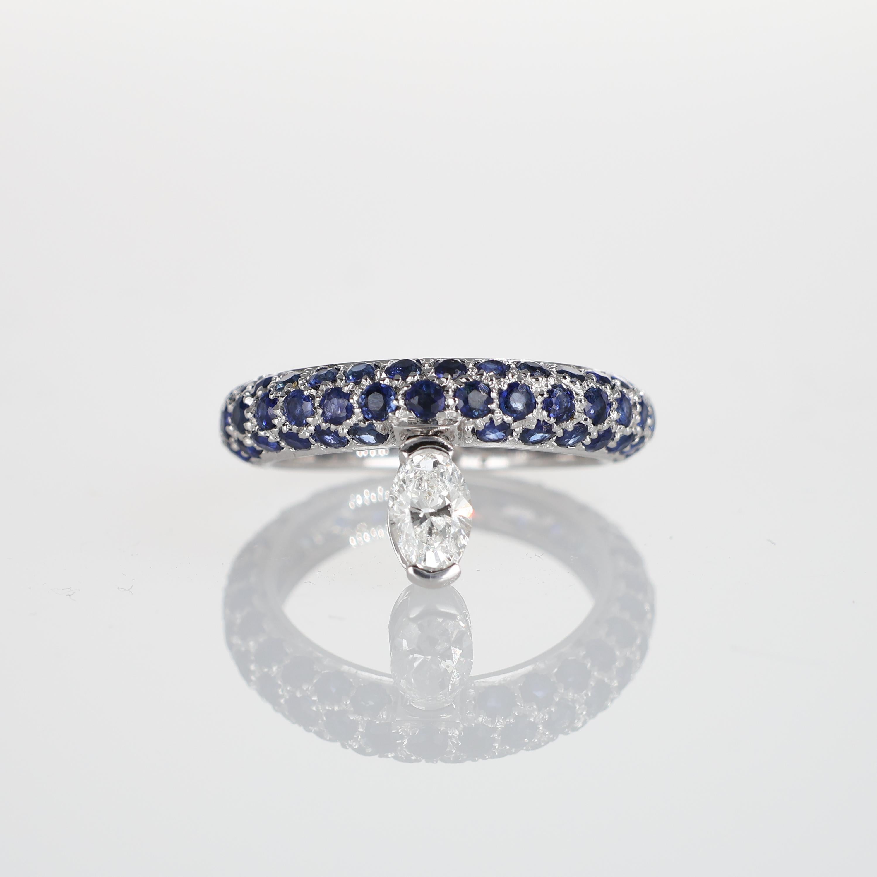 A contemporary ring crafted in 18K white gold, featuring a seamless pavé of deep blue sapphires totaling 2.8 carats. The refined setting is enhanced by a suspended natural oval-cut diamond of 0.43 carats, creating a striking interplay of color and