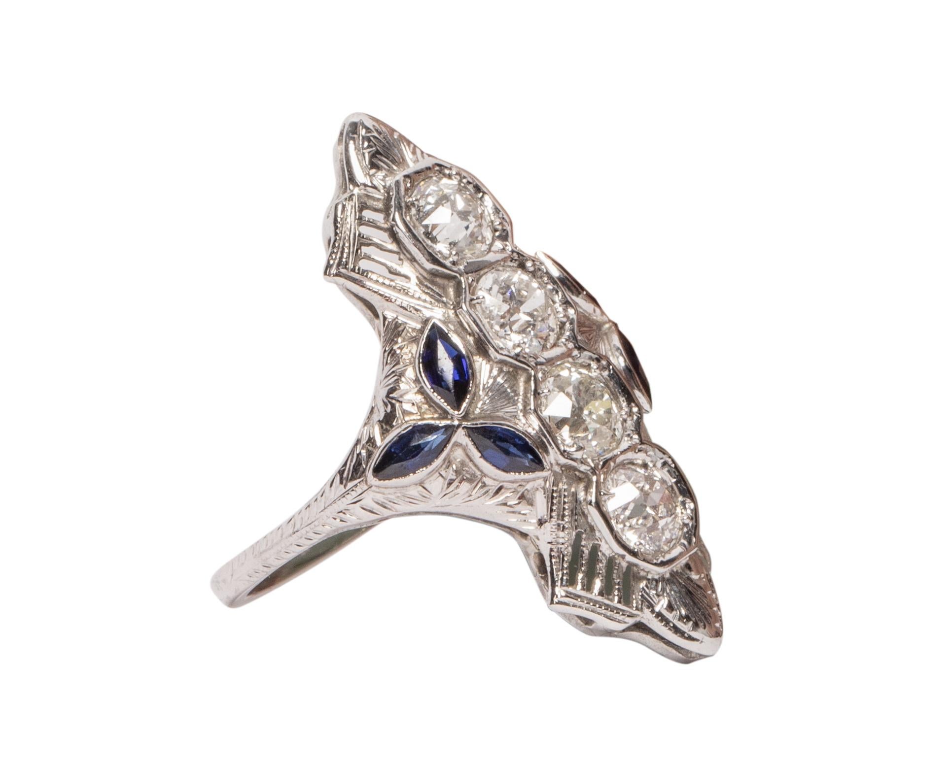 This lovely example of an Art Deco shield ring is crafted of stunning 18k white gold. Intricate filigree designs surround 3 sparkling diamonds on this vintage beauty. Two sapphire pyramids add a pop of color that adds to this already beautiful