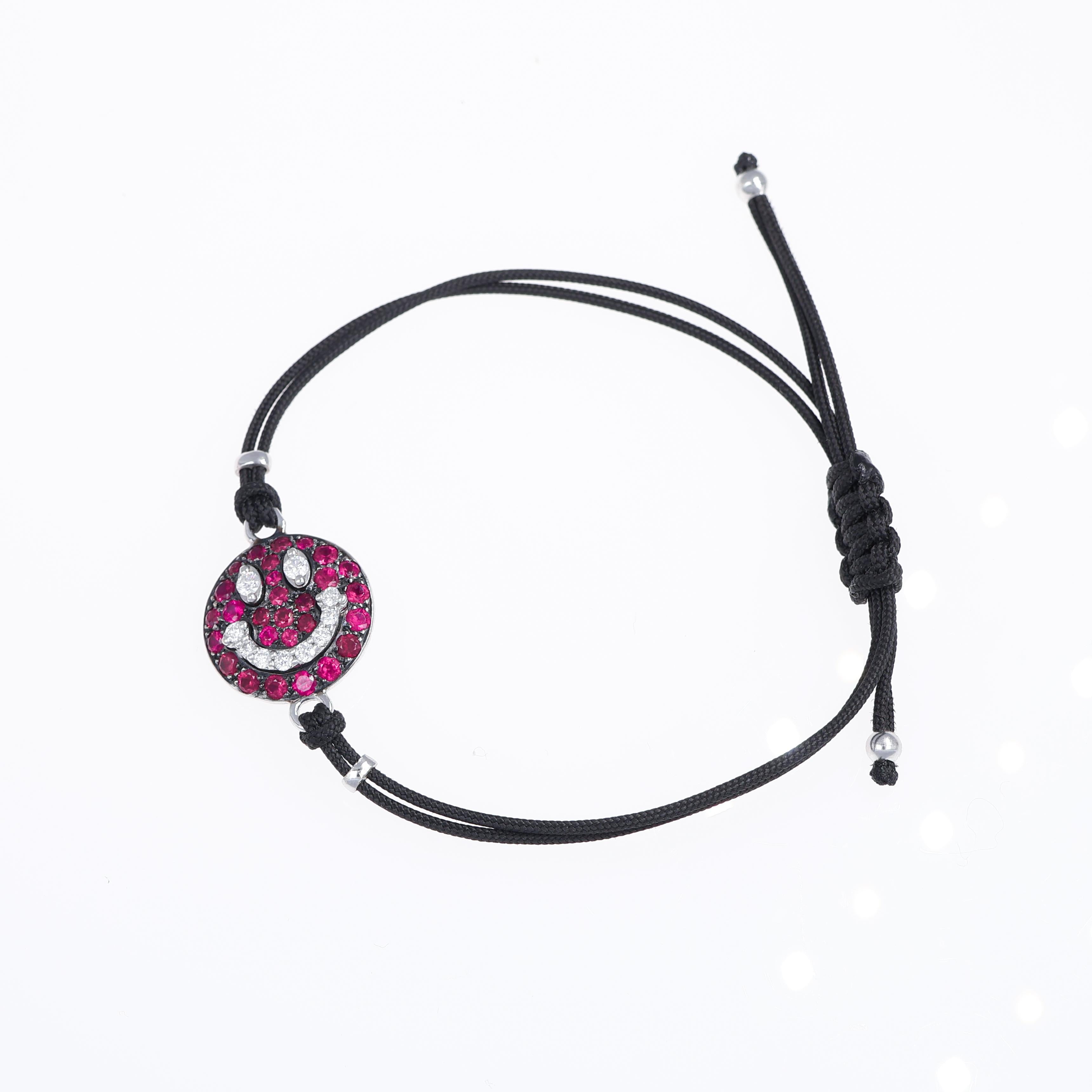 A vibrant and playful bracelet crafted in 18K white gold, featuring a smiley face motif adorned with 1.20 carats of vivid rubies and 0.26 carats of brilliant-cut white diamonds. The adjustable black cord adds a modern, casual touch, making this