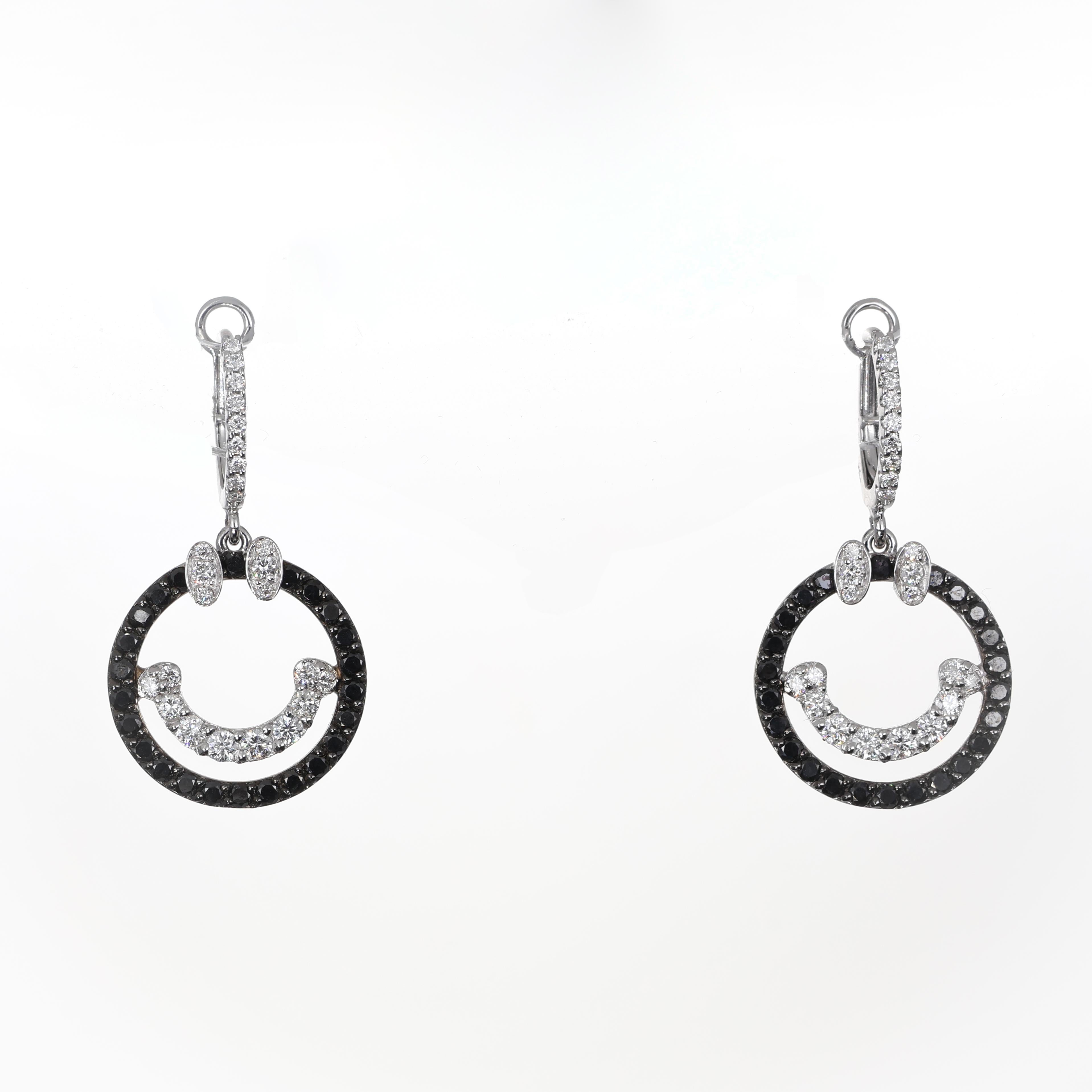A modern take on playful luxury, these 18K white gold dangle earrings showcase a captivating smiley face design, adorned with a mix of black and white brilliant-cut diamonds. The contrast between the black diamond-encrusted circle and the white