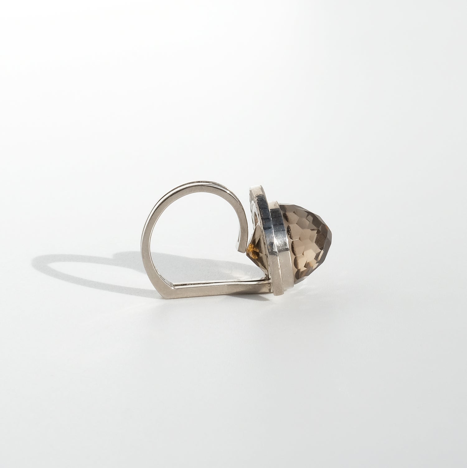 This vintage ring is crafted in 18 karat white gold, featuring a faceted smoky quartz centerpiece with a dome-like shape reminiscent of a handmade gummy candy. The stone is surrounded by a horseshoe-shaped halo set with diamonds, giving it a refined