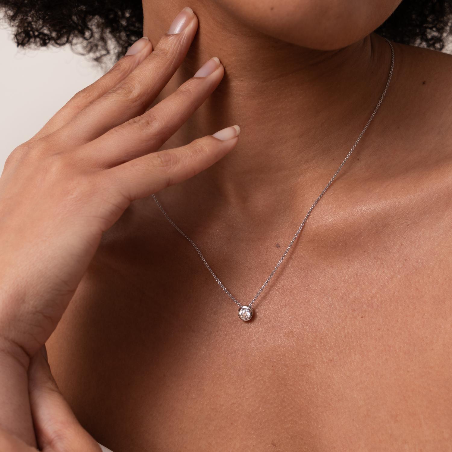 Una rivisitazione contemporanea del classico pendente con diamante solitario, con un bordo in oro bianco massiccio 18 carati che circonda la pietra. La sottile catena a forma di traccia passa attraverso l'incastonatura in modo da scorrere