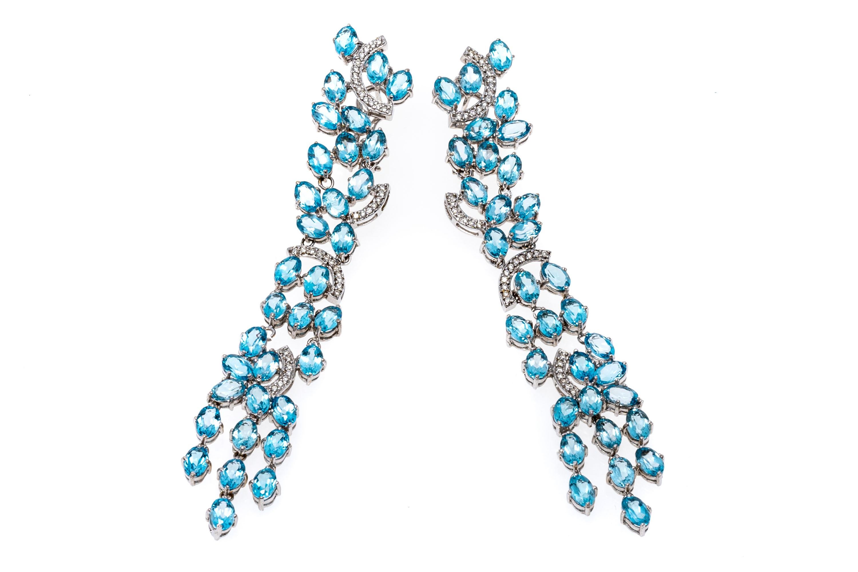 18k white gold earrings. These stunning waterfall earrings are set with long, twinkling rows of oval faceted, medium to light blue color blue topaz stones, approximately 27.06 TCW, and prong set. Scattered among the draped blue topaz are curves of