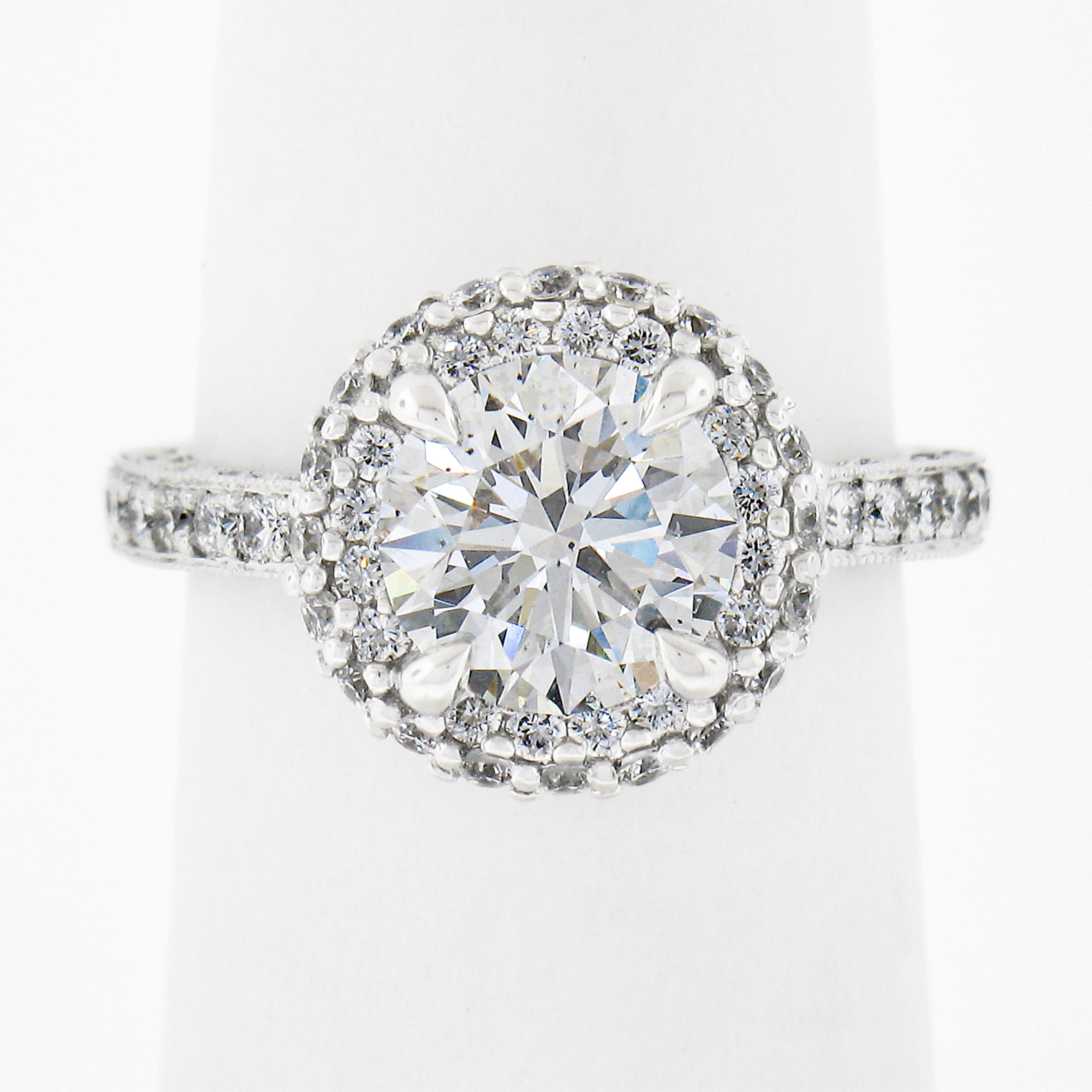 This classic and fiery engagement ring is designed by Tacori and crafted in solid 18k white gold. It features a truly breathtaking, GIA certified, round brilliant cut solitaire claw-prong set at the center of an elegantly designed halo. This center
