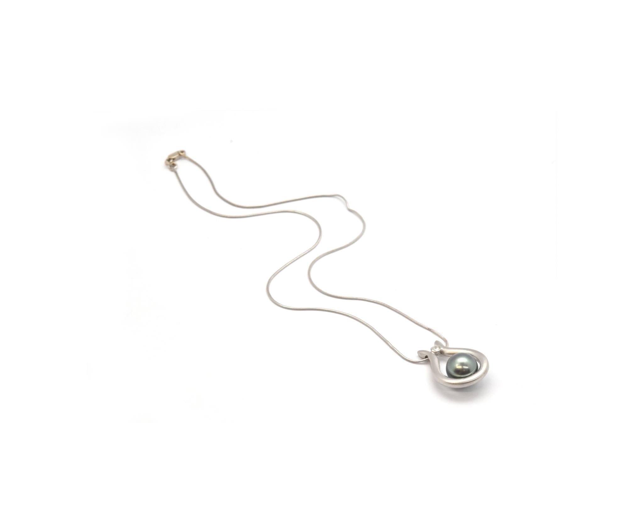 This necklace is made in 18k white gold. It features a Tahitian pearl measuring 10mm in diameter. The pearl is accented by a single diamond weighing 0.11ct. The pendant measures 18x25mm, and the necklace measures 16 inches. The necklace weighs 10.5