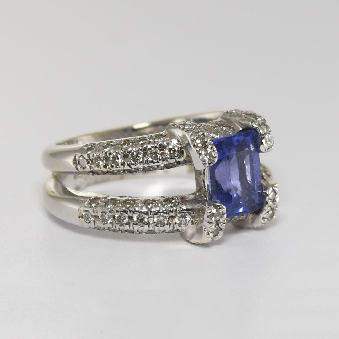 Anello da donna in oro bianco 18 carati con tanzanite e diamanti.
La tanzanite centrale da 1,5 carati è un rettangolo di colore bluastro-violetto chiaro o medio.
I diamanti laterali sono rotondi e brillanti e hanno un peso totale di 1,00