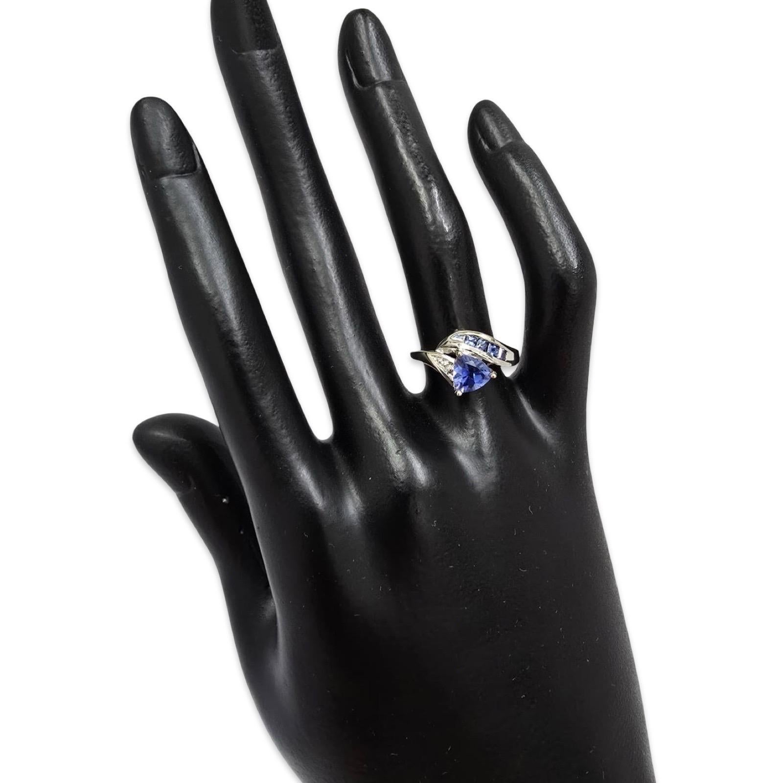 Cette bague moderne en or blanc massif 18 carats est sertie d'un saphir brillant de taille trillion d'un bleu royal éclatant. La pierre centrale est rehaussée d'un élégant canal de saphirs bleus carrés qui s'étendent harmonieusement le long de