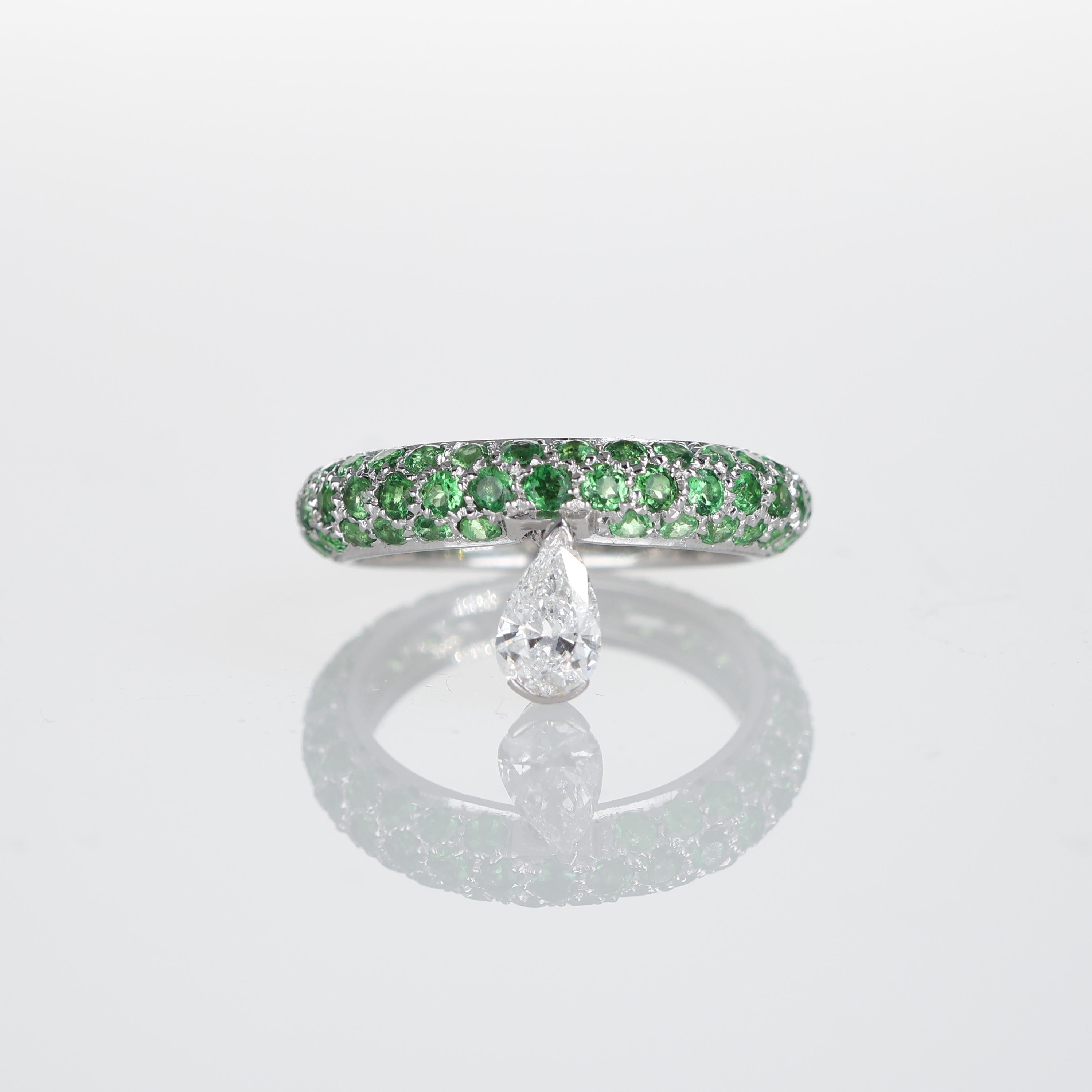 A distinctive band ring crafted in 18K white gold, adorned with a pavé of vibrant tsavorites totaling 2.22 carats. A suspended 0.46-carat pear-cut brilliant diamond adds movement and an unexpected touch of elegance. The contrast between the deep