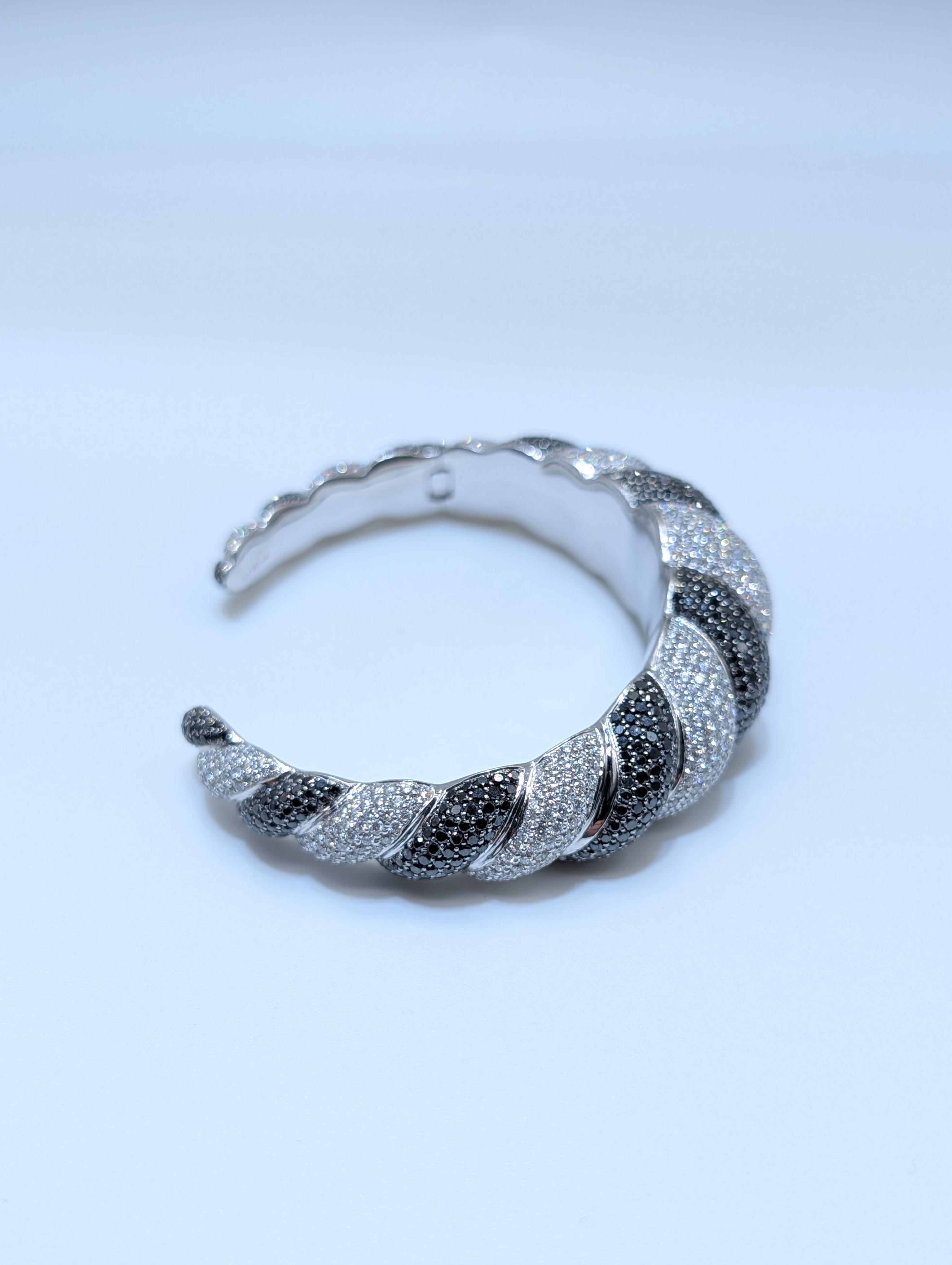 Audace ed elegante, questo splendido bracciale a torciglione è magistralmente realizzato in oro bianco 18 carati e impreziosito da un'abbagliante serie di diamanti bianchi e neri per un totale di ben 17 carati. Il sofisticato design alternato mette