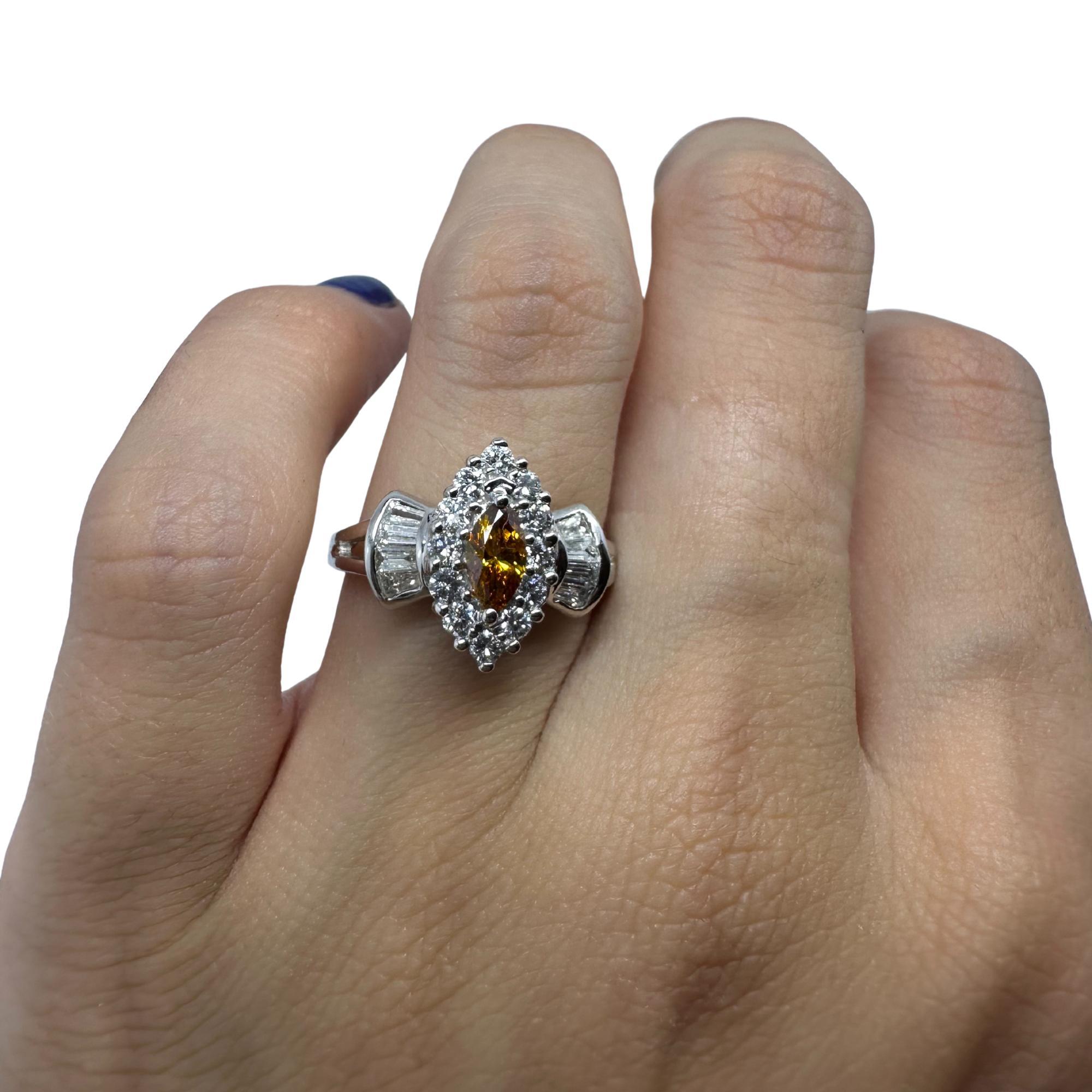 Questo anello con diamante è realizzato in oro bianco 18 carati e progettato in un grazioso stile navette. Al centro si trova un diamante giallo taglio marquise, la cui forma allungata attira lo sguardo e irradia una calda tonalità dorata. Il centro