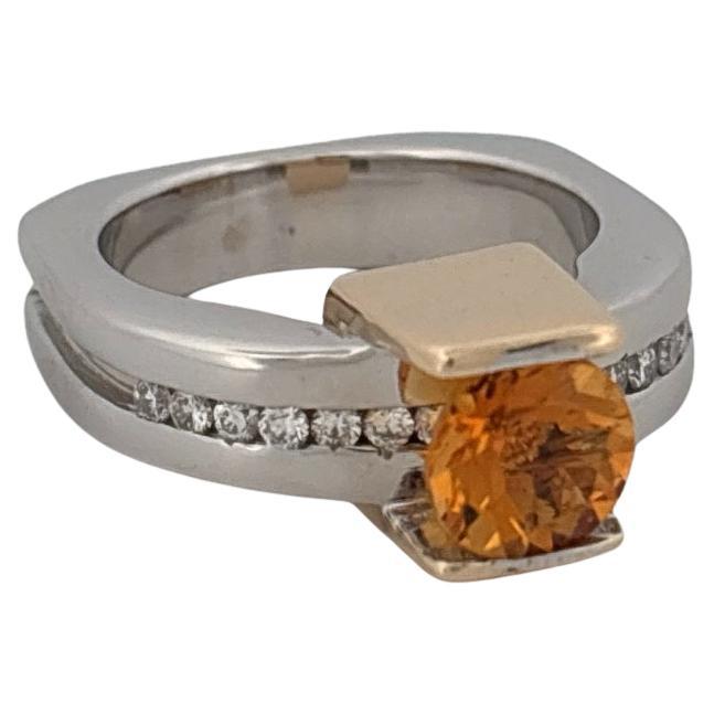 This striking contemporary ring is crafted in 18k white and yellow gold, showcasing an architectural, modernist design. At its center rests a vivid 1.10 carat round-cut citrine, bezel-set in a sleek yellow gold frame that adds warmth and contrast to