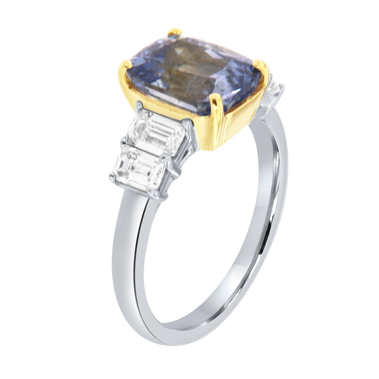This stunning ring features a violetish blue 3.55 Carat Sri-Lankan Sapphire set in an 18k Yellow gold cup flanked by four emerald shape diamonds, 0.90-carat total weight, F in color, and VS1 in clarity on an 18k white gold 2.4 mm band. The sapphire