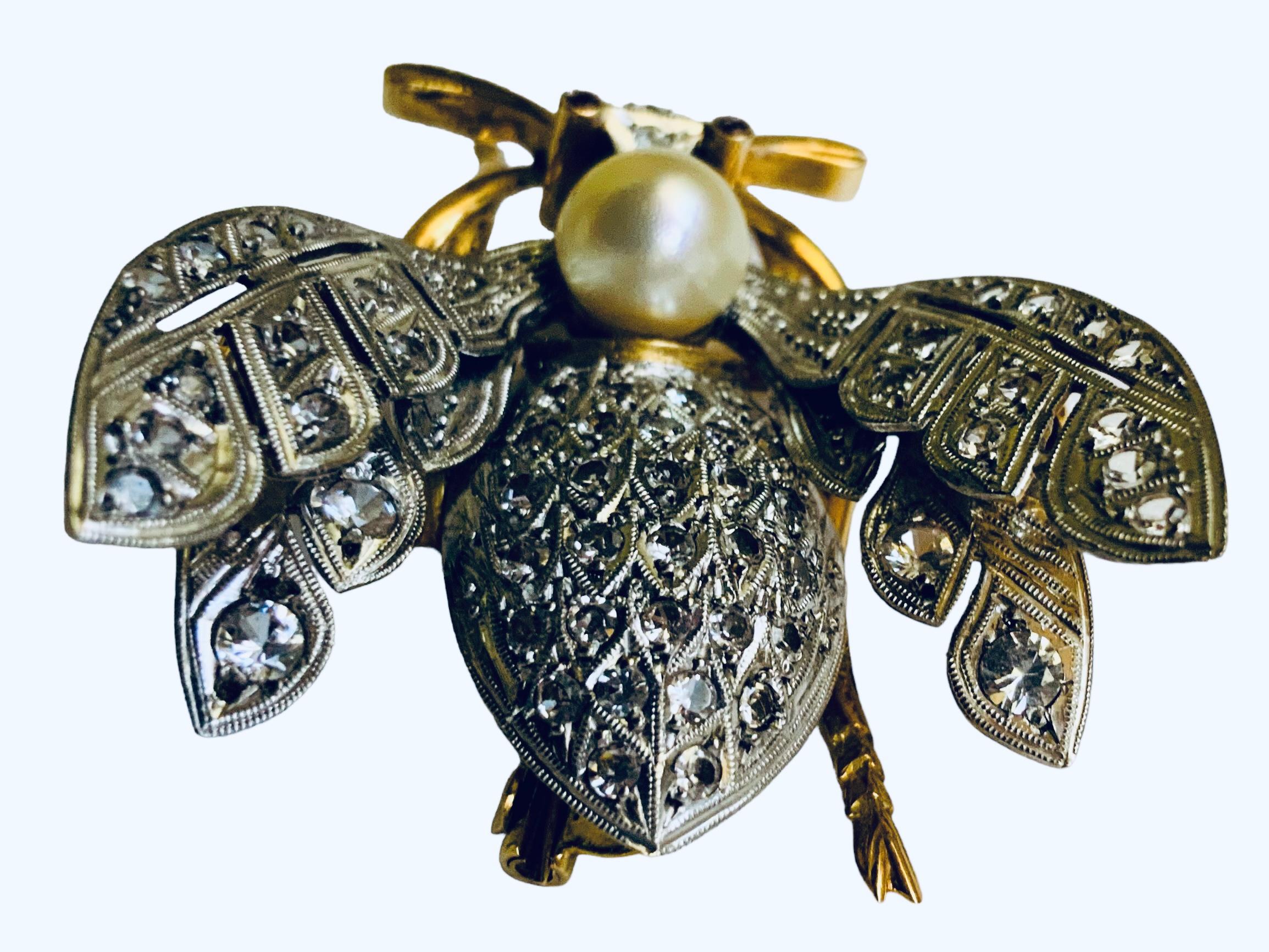 This is an 18K White and Yellow Gold Diamonds, Pearl and Rubies Insect Brooch. A very well done brooch that depicts a large bee body and wings adorned with a cluster of sparkling tiny diamonds in pave setting. The head of the bee is made by a round