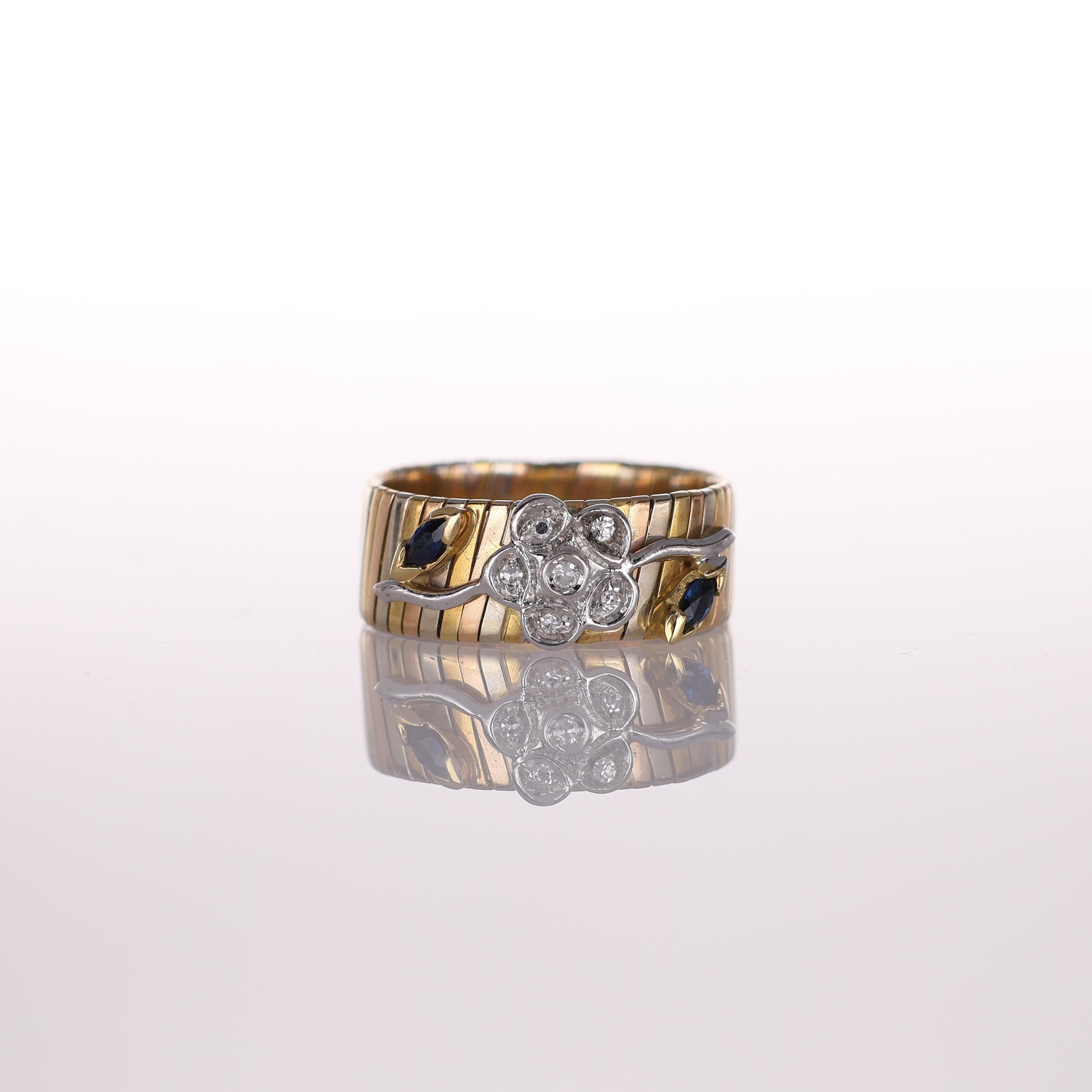 A charming band ring crafted in 18K yellow and white gold, featuring a delicate floral motif adorned with 0.10 carats of brilliant-cut diamonds and accented by deep blue sapphires. The intricate design blends vintage inspiration with timeless