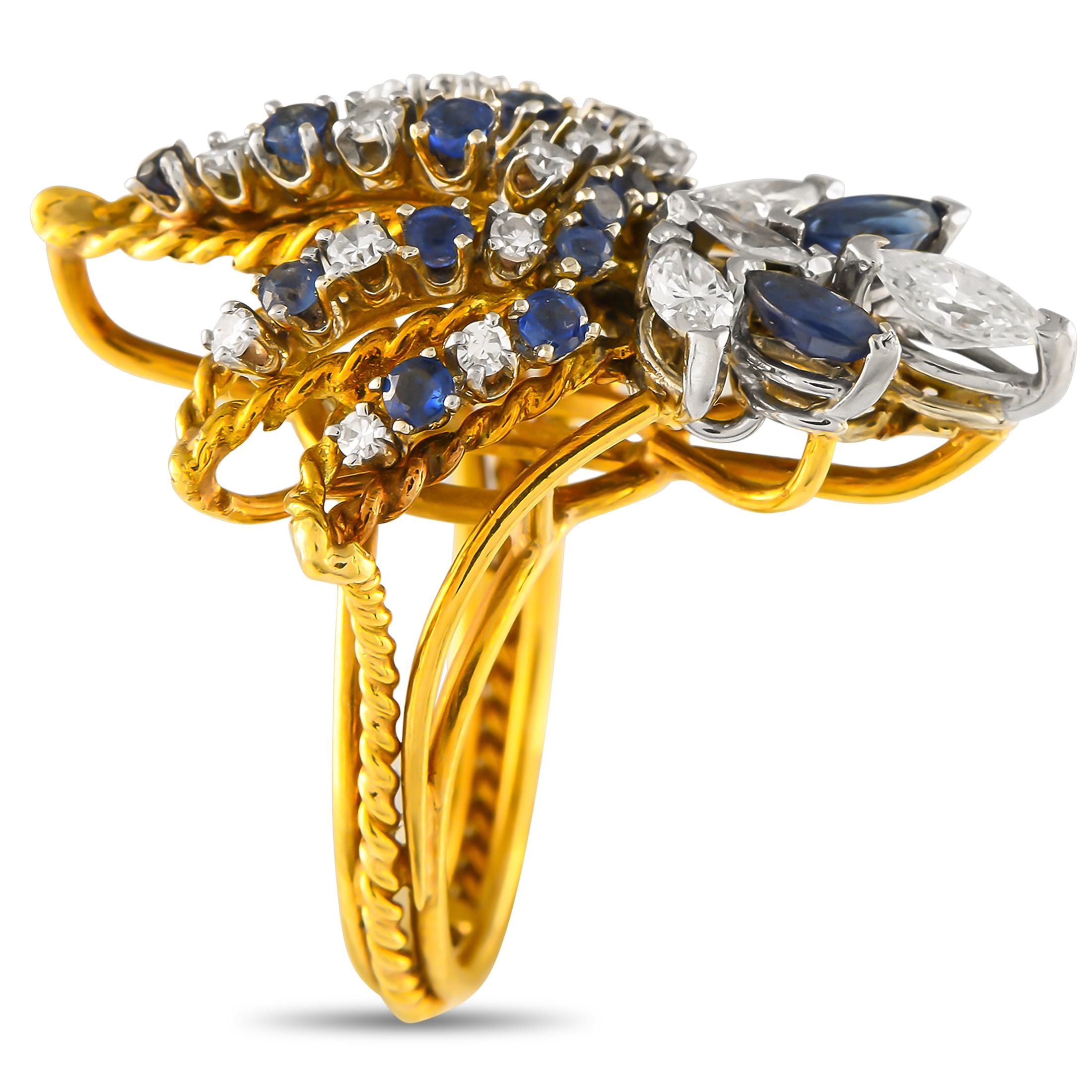 Questo anello in oro giallo, che emana una bellezza regale, è disegnato ad arte con dettagli delicati e intricati. Questo pezzo edoardiano è caratterizzato da un centro a forma di fiore, punteggiato da un'alternanza di zaffiri e diamanti. I bordi a