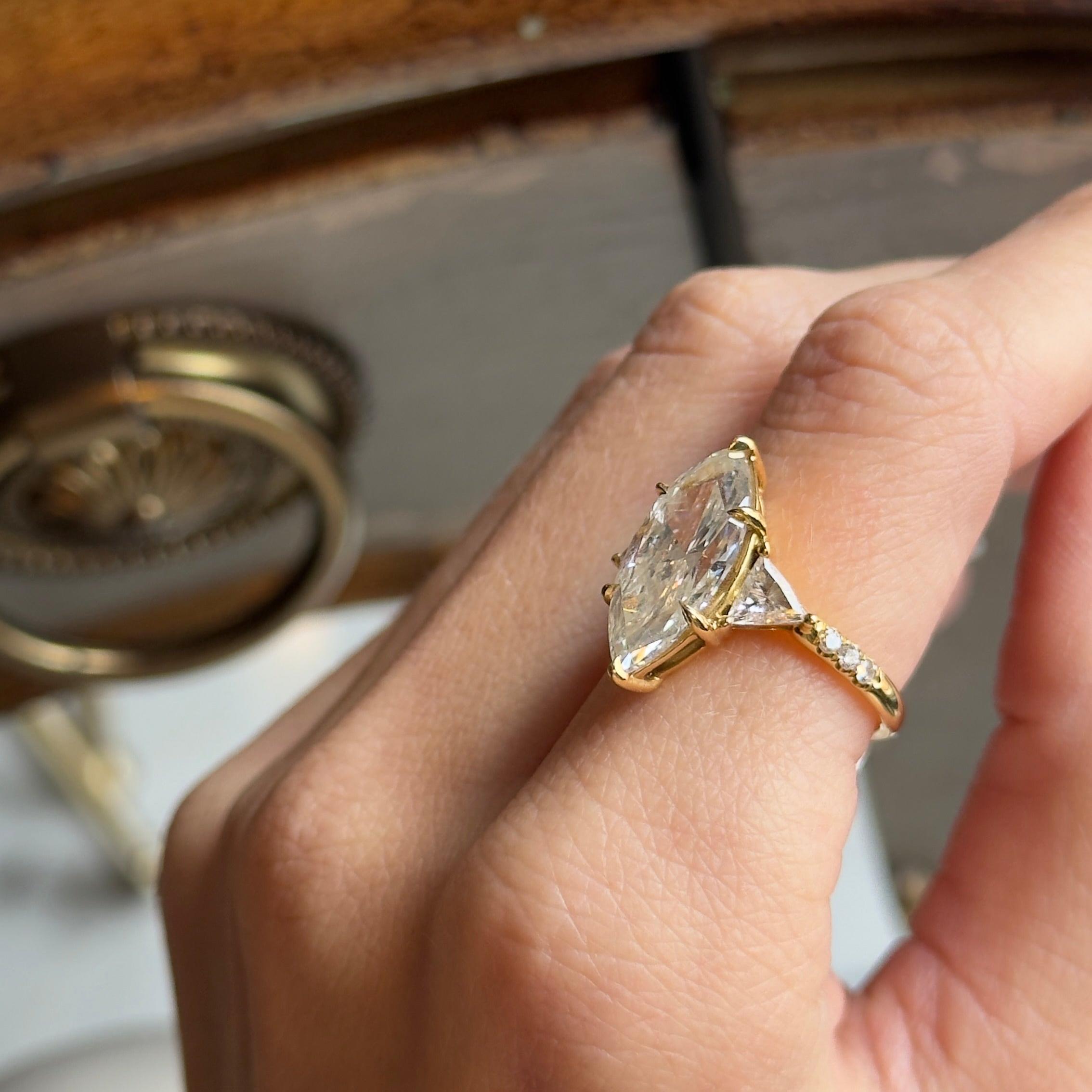 Époque : New 

Composition : Or jaune 18K

Pierre principale : Diamant taillé en marquise

Poids en carats : 4,05 carats

Couleur/ Clarté : J / I1

Numéro de rapport GIA : 6173554969

Pierre d'accentuation : Deux diamants taillés en trillion

Poids