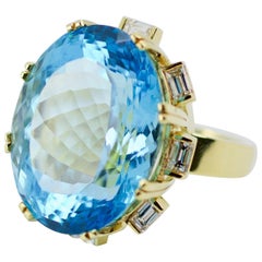 18 Karat Gold 66 Carat Oval Blue Topaz with a Halo of Emerald Cut Diamond Ring