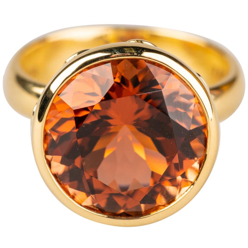 An 18k yellow gold ring set with one round 9.74 carat orange and pink tourmaline, 13.77mm. RIng size 6.5. This ring was made and designed by llyn strong.