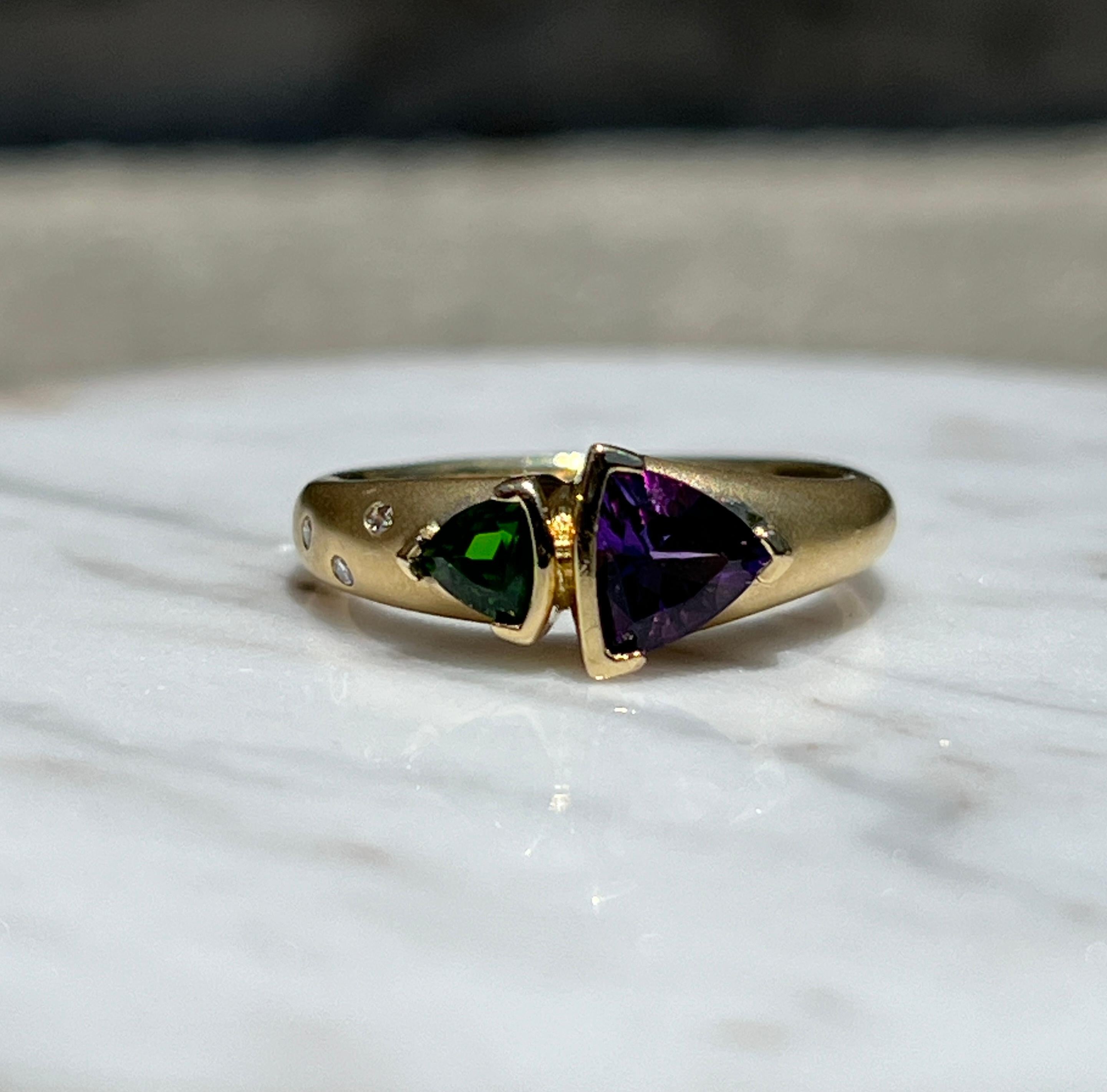 Dieser Ring aus den 1990er Jahren ist aus 18 Karat mattem Gelbgold gefertigt und zeigt einen auffälligen Amethysten im Billionen-Schliff (ca. 0,66 Karat), gepaart mit einem leuchtenden Chromdiopsid im Billionen-Schliff (ca. 0,27 Karat). Der Ring ist