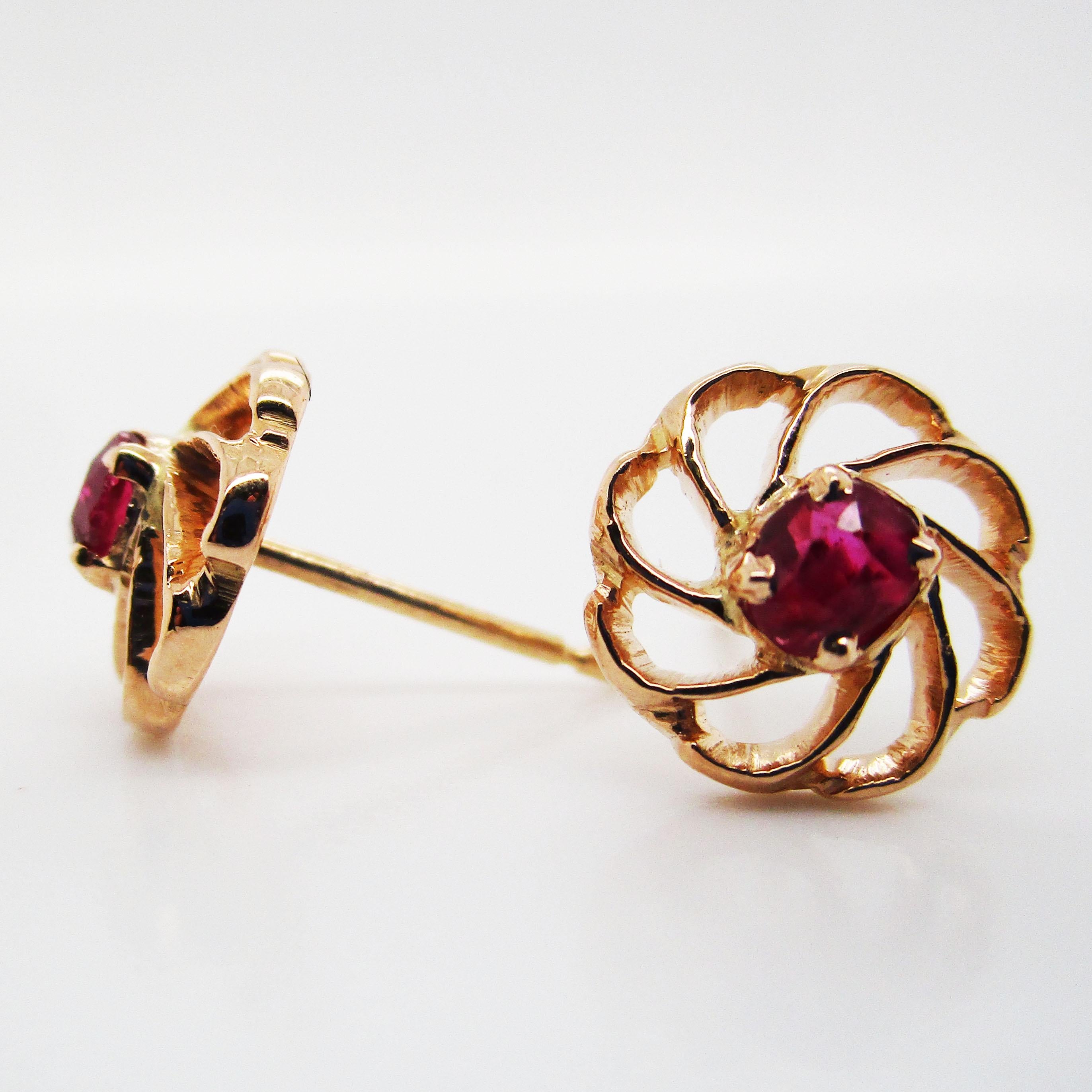 Brilliant 18 karat yellow gold and stunning deep red rubies come together to create a enchantingly alluring pair of vintage stud earrings. The 18k yellow gold twists in a beautiful design that evokes a nautilus shell theme, similar to a love knot.