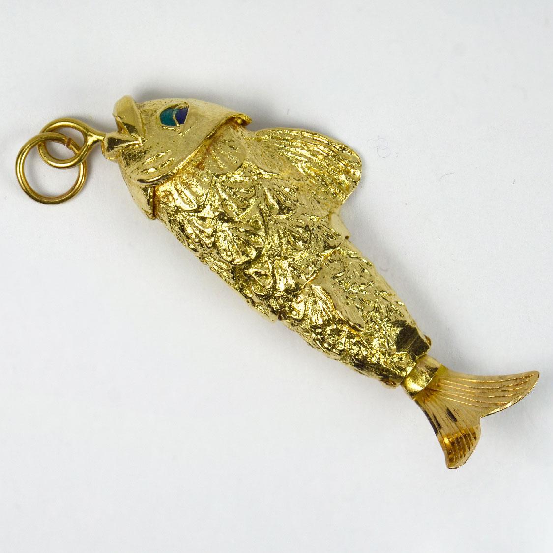 An 18 karat (18K) yellow gold charm pendant designed as a fish with an articulated flexible tail and enamel eyes. Unmarked but tested for 18 karat gold.

Dimensions: 5.9 x 1.9 x 1.05 cm (not including jump ring)
Weight: 14.78 grams 
