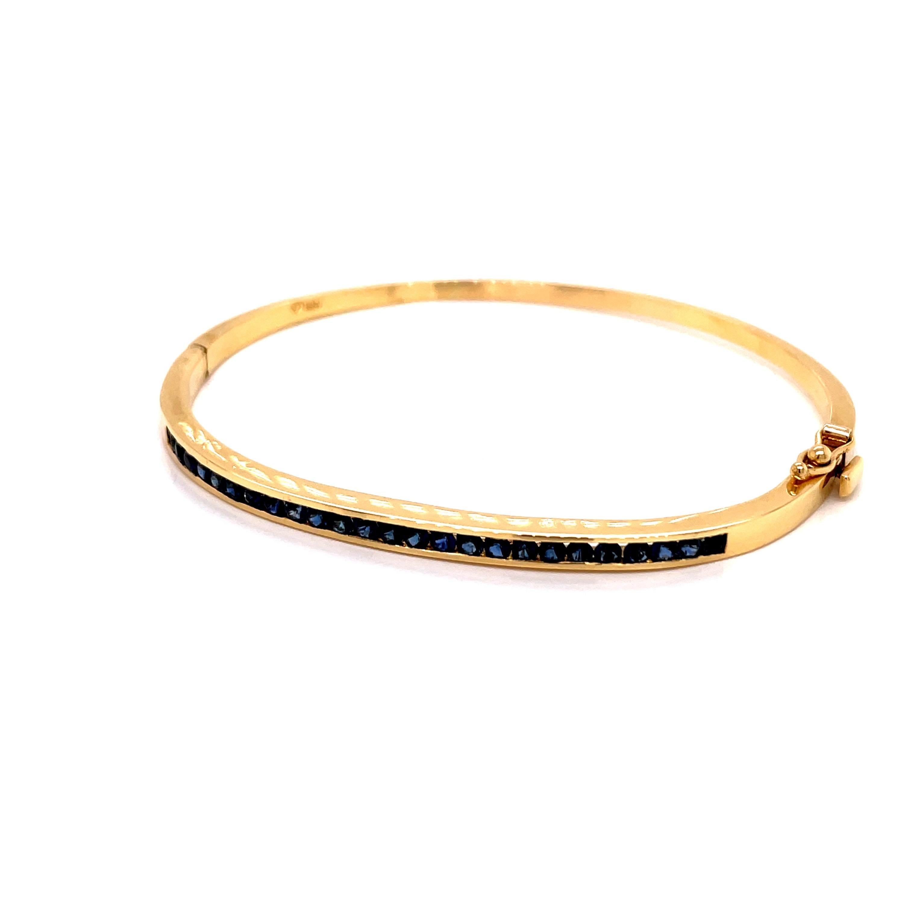 18K Yellow Gold Bangle Bracelet Channel Set Sapphires - The bangle contains 25 round sapphires weighing approximately 1.50ct. The bangle measures 3.6mm wide on the top and 2.3mm wide on the bottom. The inside diameter is 2.12 inches high and 2.5