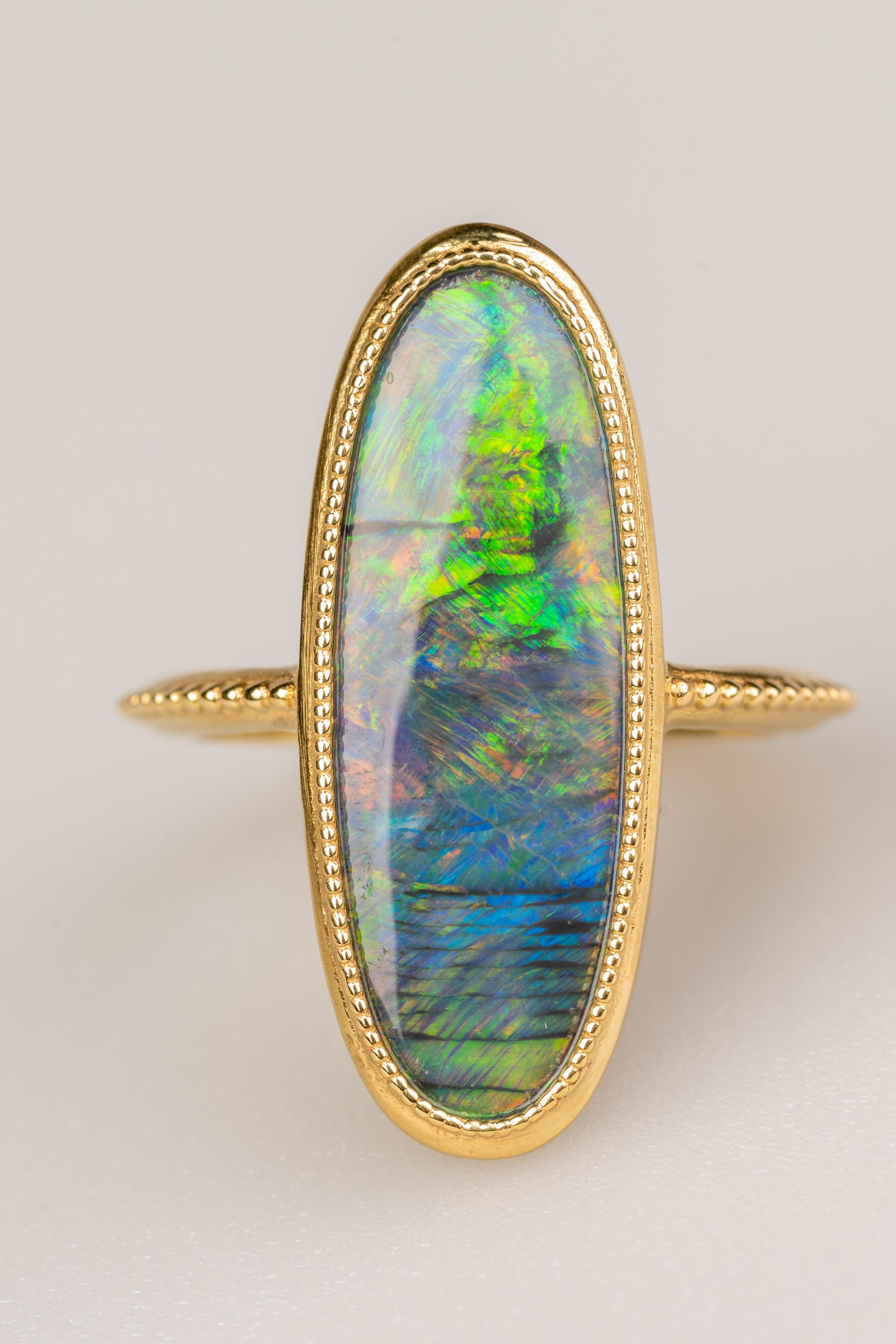 An 18k yellow gold ring featuring one bezel set oval freeform Lightning Ridge Australian black opal 3.83 carats and accented with bead work around the ring. Ring size 6.5. This ring was designed and made by llyn strong.